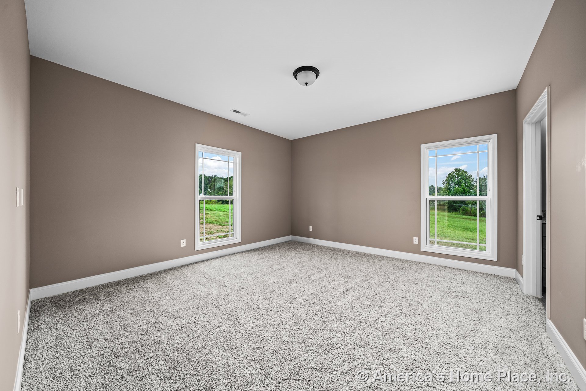 Bedroom with two large windows, beige painted walls, plush carpet flooring, white baseboards, flush mount ceiling light, and trimmed doorway.
