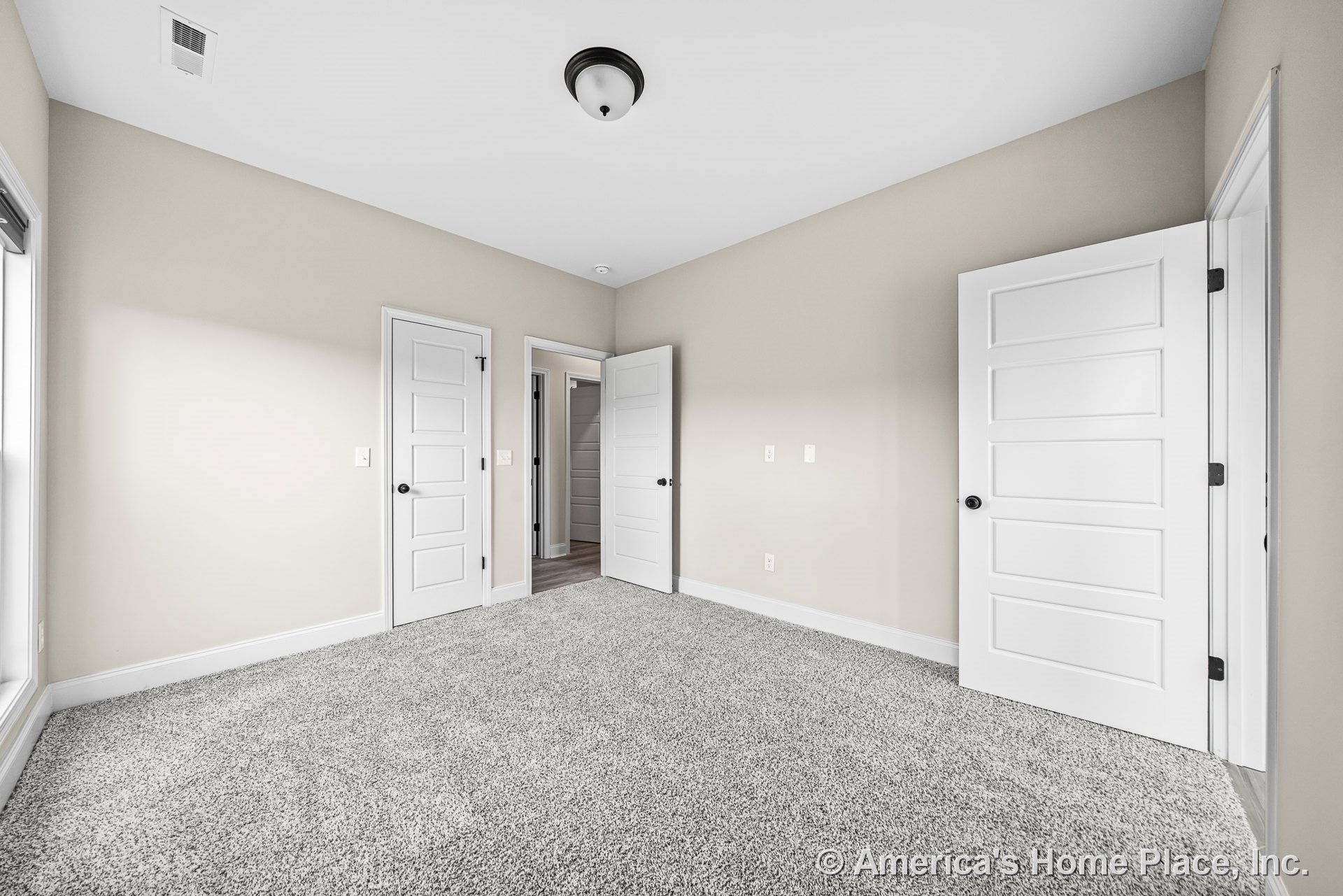 Bedroom with light gray carpet flooring, beige walls, three white paneled doors, white baseboard trim, flush mount ceiling light, and large window.
