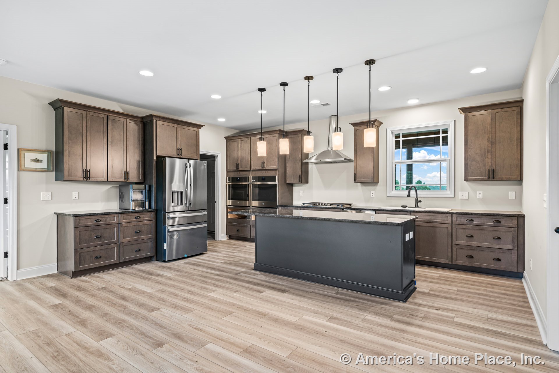 Wood shaker cabinets and built-in cabinetry surround a central kitchen island with granite countertops, stainless steel refrigerator, double wall ovens, range hood, undermount