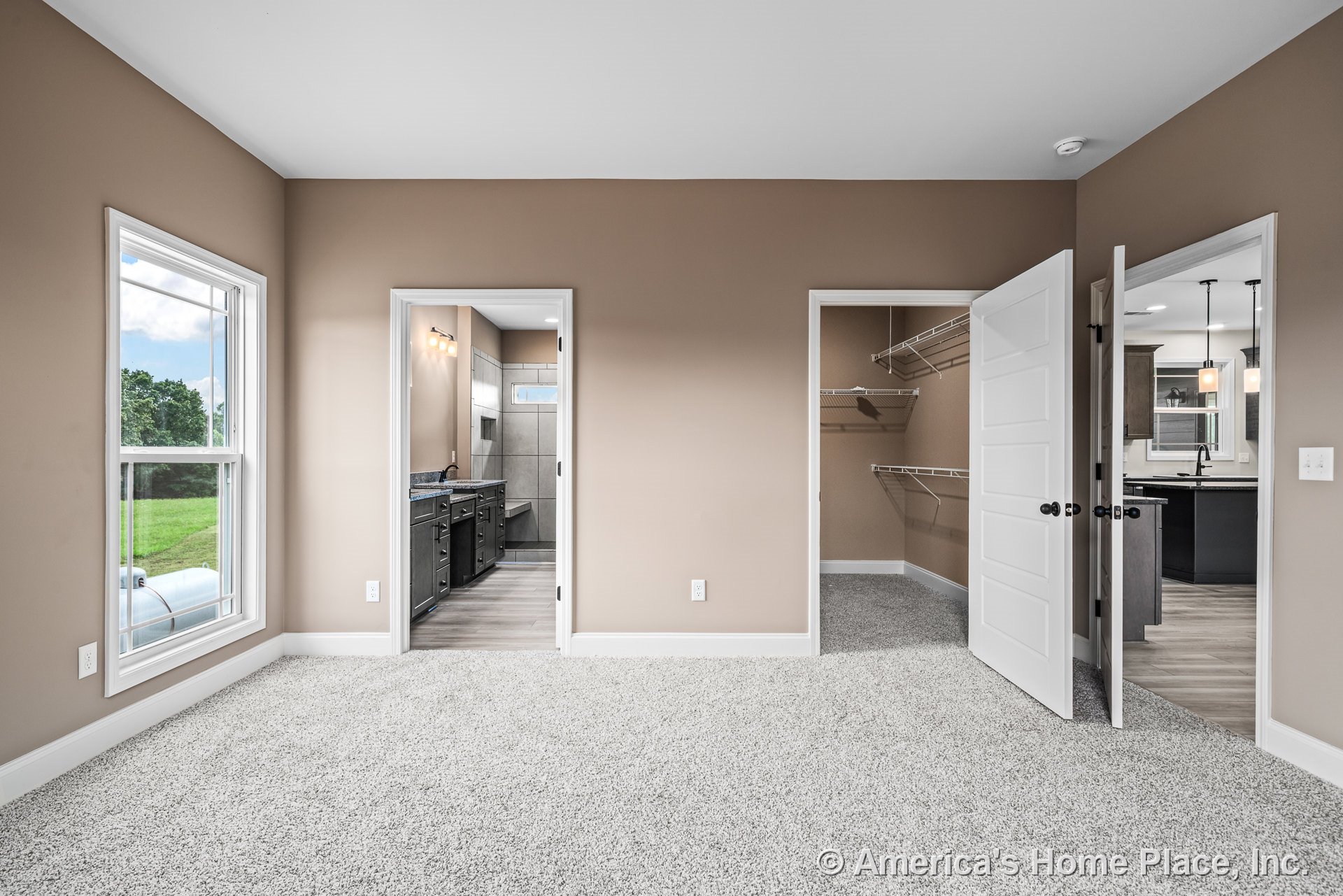 Bedroom with beige walls and carpet flooring, walk-in closet featuring wire shelving, en suite bathroom with tile walls and dark cabinetry, large window with white trim, and white