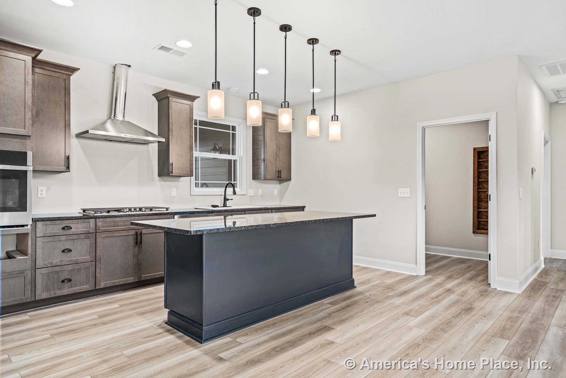 Central kitchen island with dark wood cabinetry, granite countertops, stainless steel range hood, pendant lights above, window above sink, and light wood flooring.