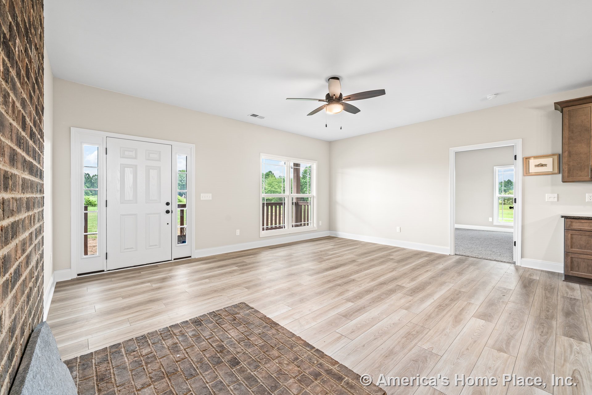 Light wood-look flooring and a brick fireplace hearth anchor the living room, which includes a ceiling fan with integrated lighting, entry door with sidelights, large double