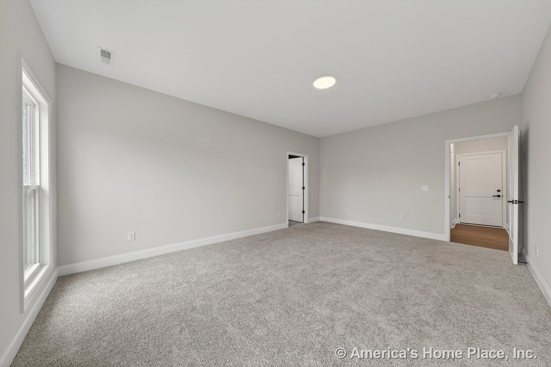 Bedroom with light gray carpet, neutral painted walls, large window with white casing, white baseboards, flush mount ceiling light, and paneled interior doors.