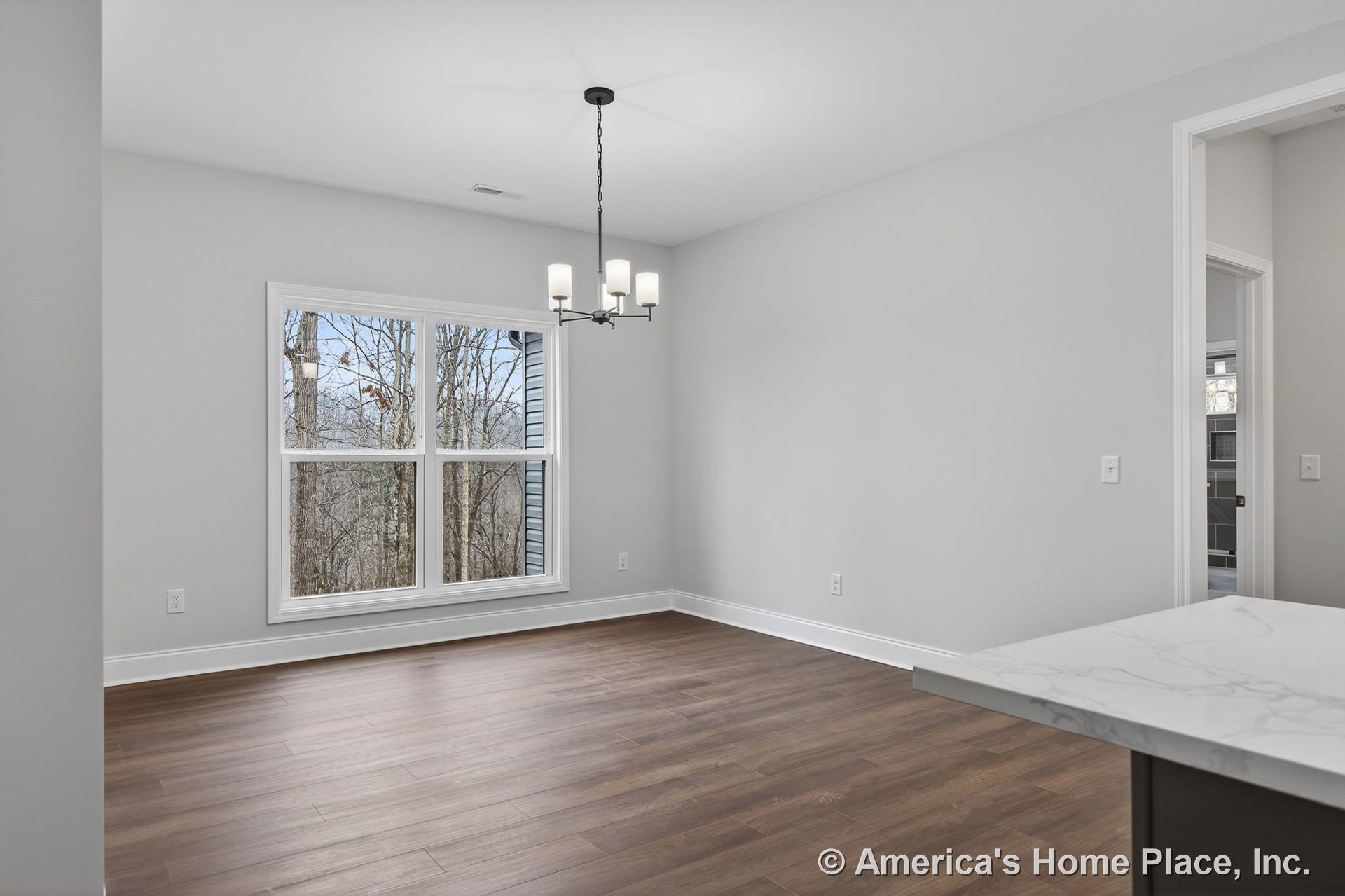Dining area with large double windows, wood-look plank flooring, modern ceiling chandelier, white trim and baseboards, open doorway to adjacent room, marble-look countertop edge