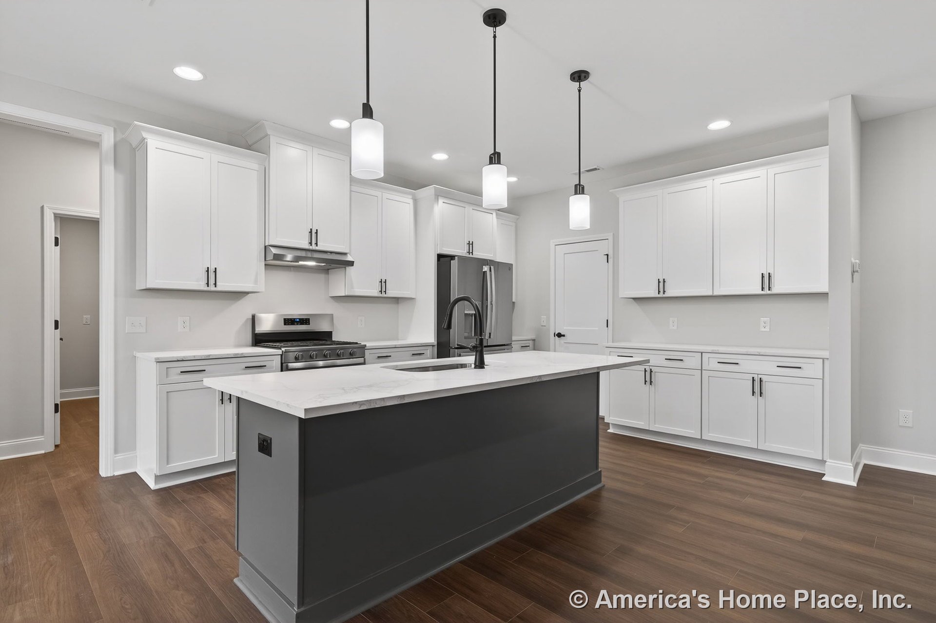 White shaker cabinets and stainless steel appliances surround a dark kitchen island with built-in sink, marble-look countertops, modern pendant lights, wood-look flooring, and