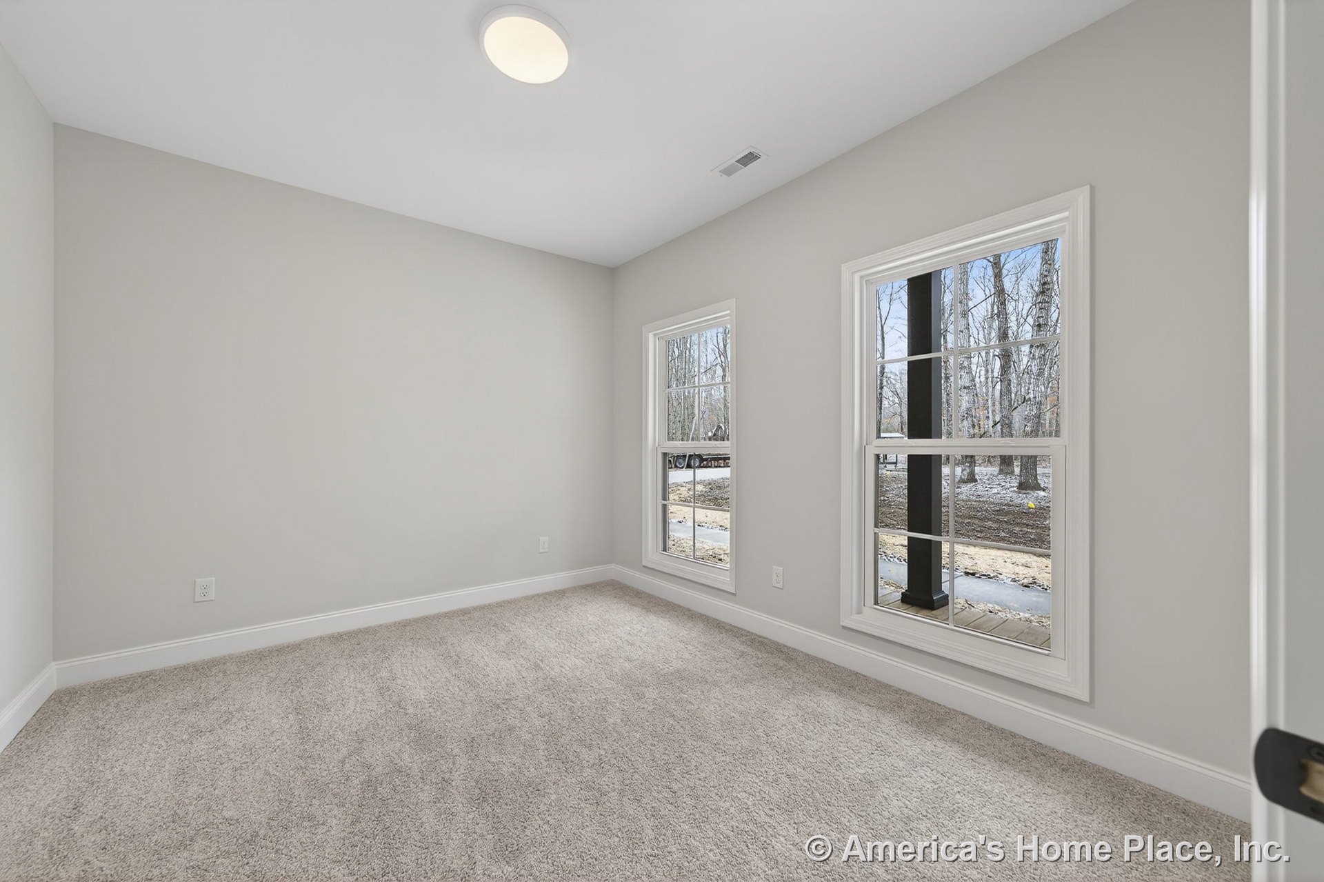 Bedroom with large double windows framed in white trim, neutral carpet flooring, flush mount ceiling light, light gray painted walls, and white baseboards in a rectangular layout.