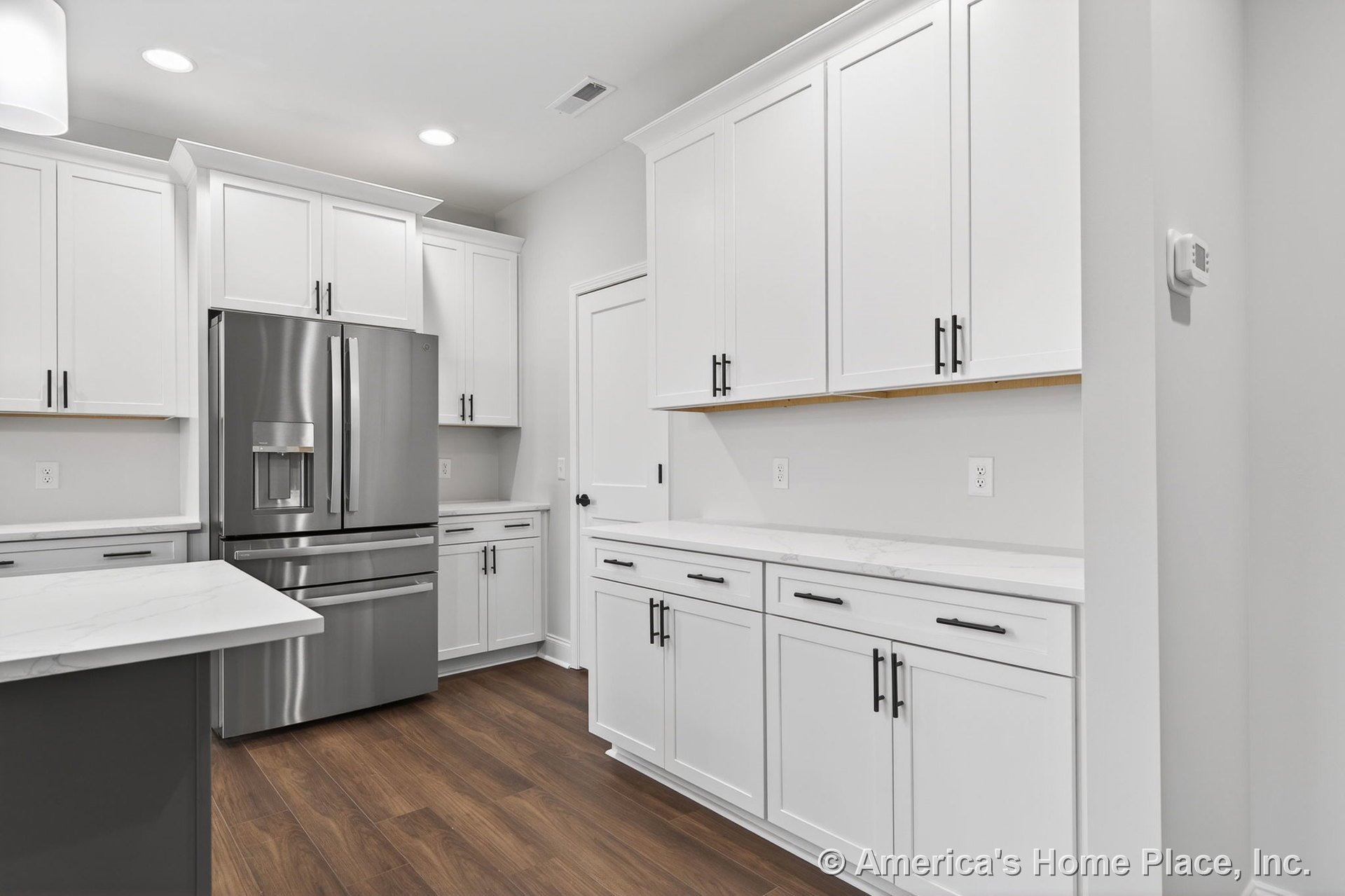 White shaker cabinets with modern hardware, marble-look countertops, stainless steel refrigerator, recessed ceiling lights, wood-look flooring, pantry door, and detailed trim.