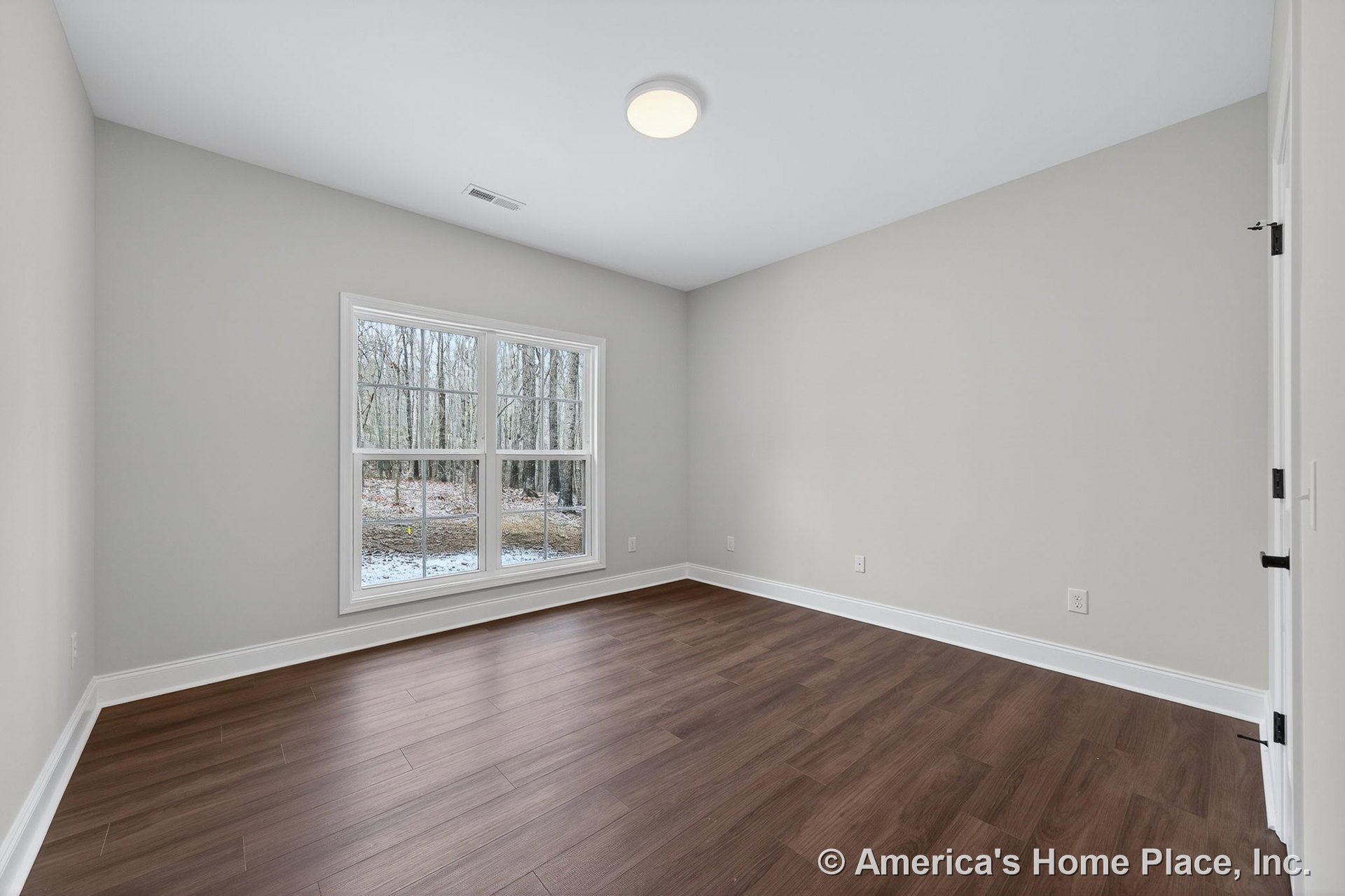 Wide plank wood flooring, large double window with white trim, neutral wall color, flush mount ceiling light, and white baseboards in a modern bedroom.