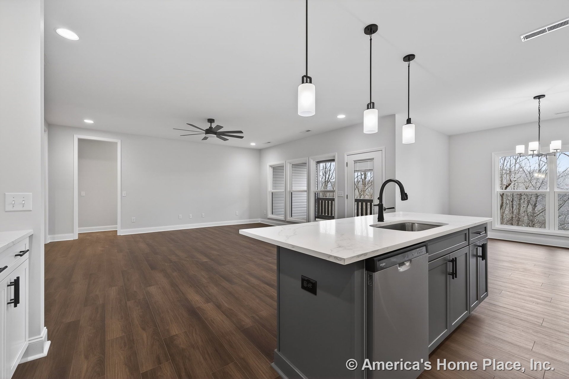 Open kitchen with a large quartz island, gray cabinetry, pendant lights above the island, wood-look flooring throughout, expansive windows, and a ceiling fan in the adjacent living