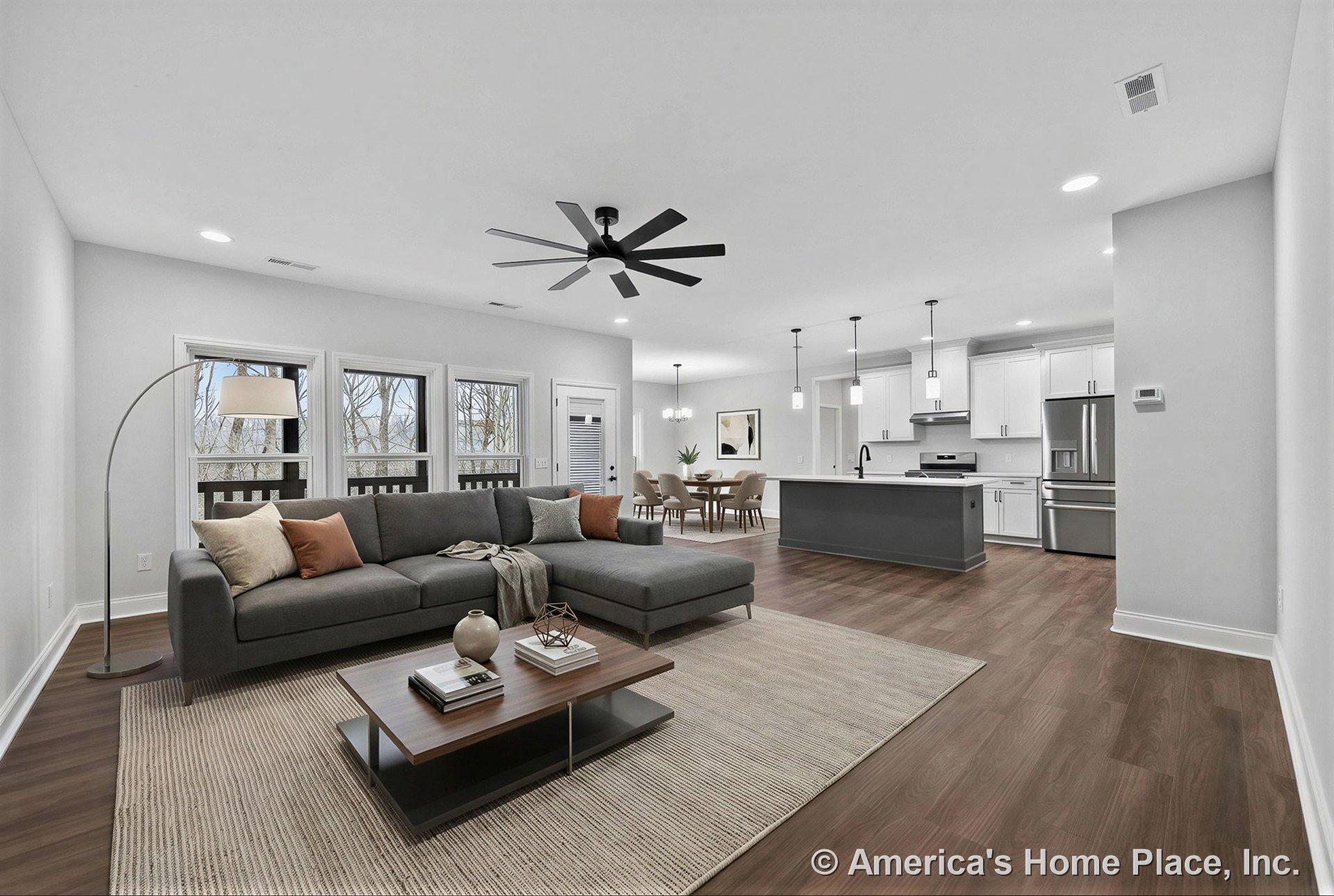 Open concept living area with dark wide plank wood flooring, three large windows, modern ceiling fan, recessed lighting, and kitchen featuring white shaker cabinets, pendant