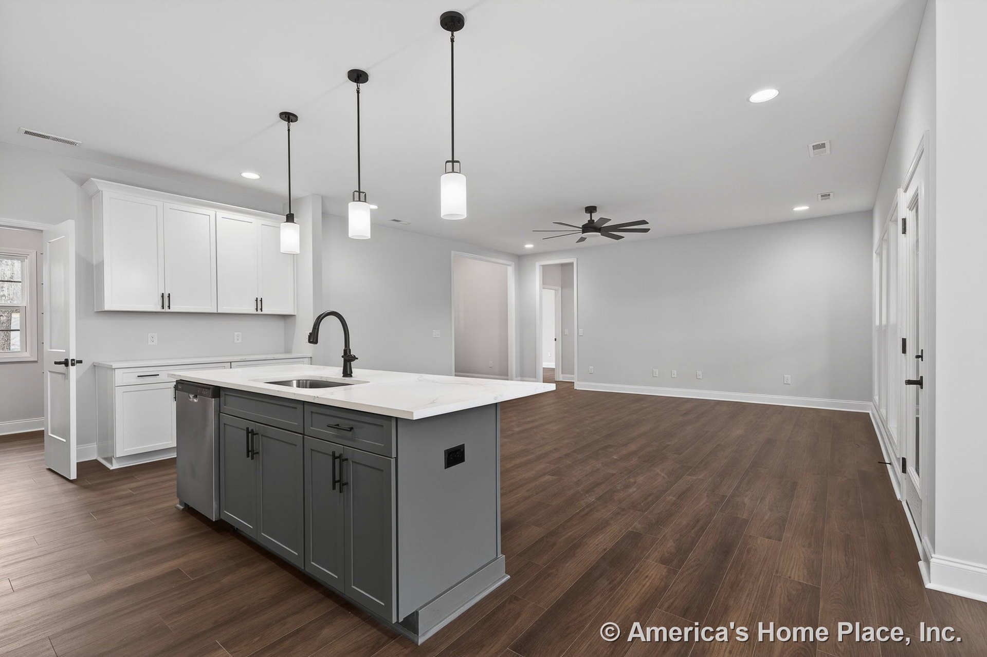 Open floor plan kitchen and living area with gray central island featuring built-in sink and quartz countertop, white upper and lower cabinetry, wood-look plank flooring, pendant