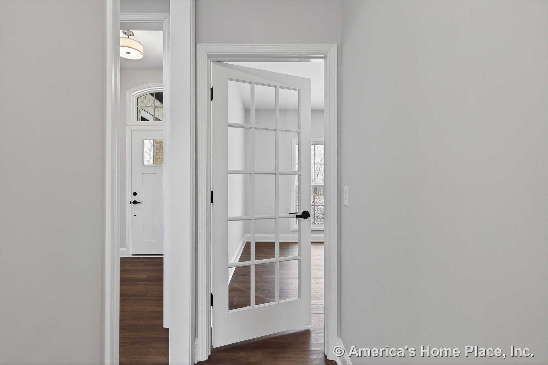 Hallway with glass-paneled interior door, white trim, hardwood flooring, entryway sidelights, large windows, neutral wall color, modern light fixture, and detailed baseboards.