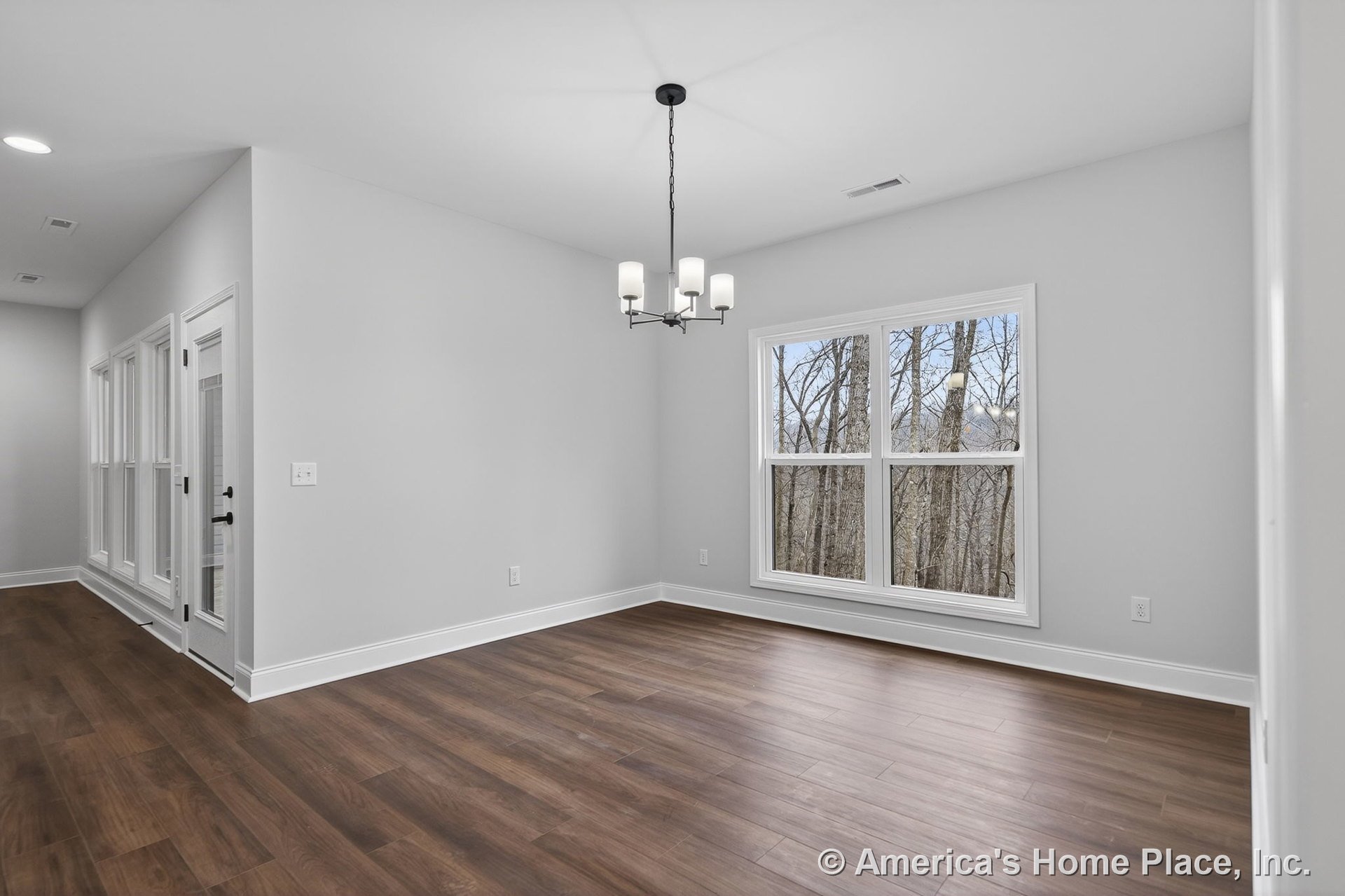 Dining area with large double window, wood-look plank flooring, white trim and baseboards, modern ceiling light fixture, glass door with sidelights, and neutral wall color.