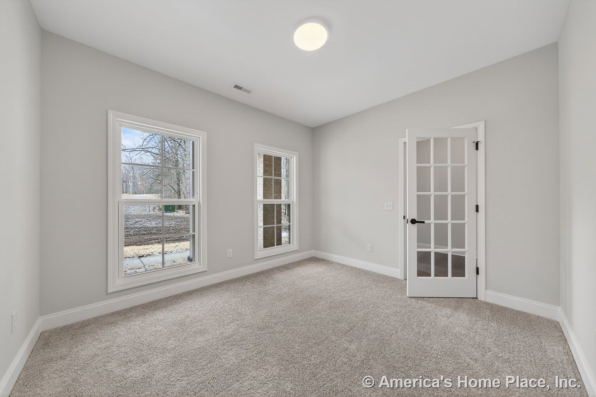 Carpeted room with neutral walls, white trim and baseboards, two double hung windows, glass-paneled French door, flush mount ceiling light, and modern door hardware.