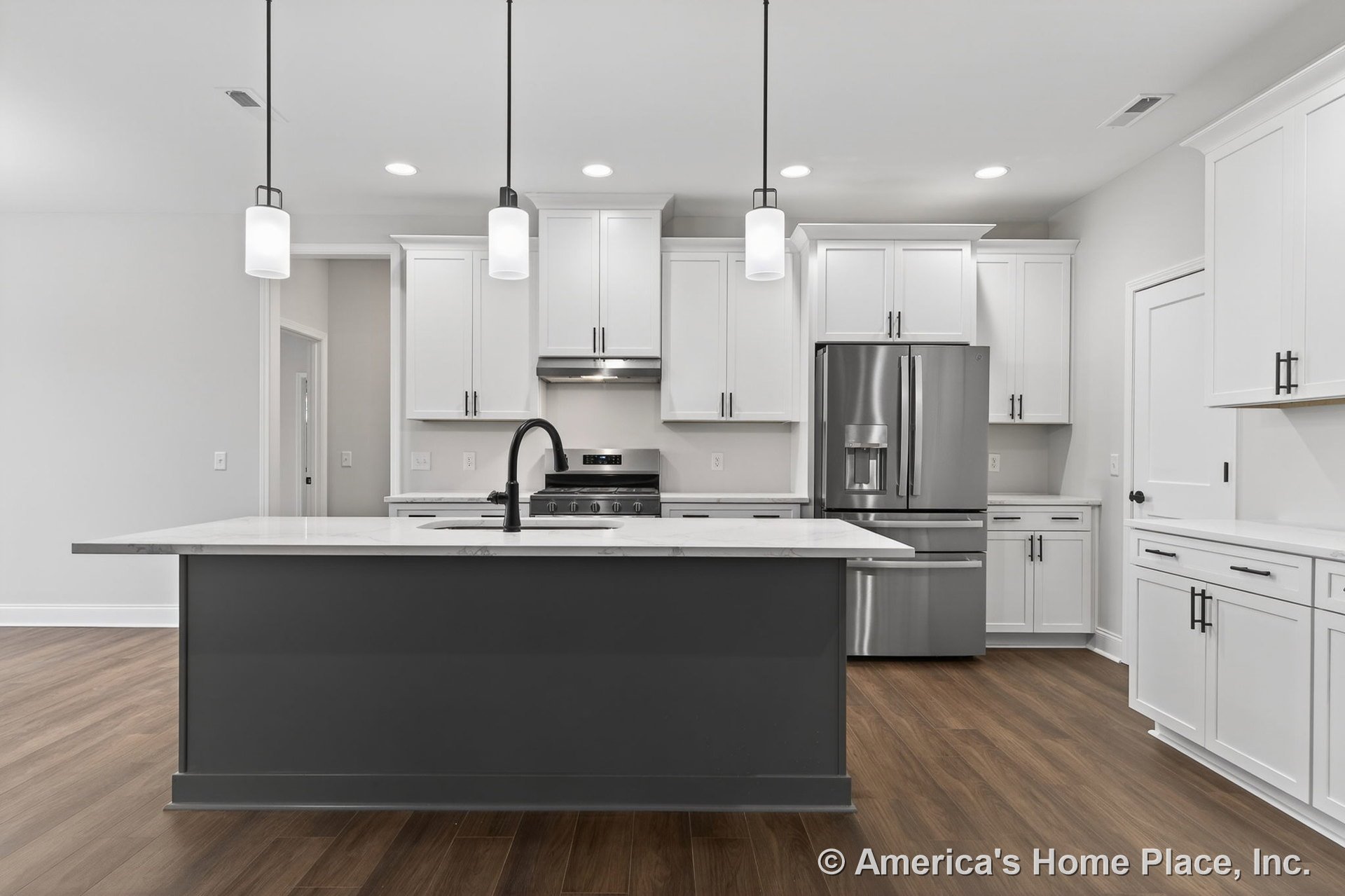 White shaker cabinets and a large gray island with quartz countertop, stainless steel appliances including built-in refrigerator and range hood, pendant lights above island, black