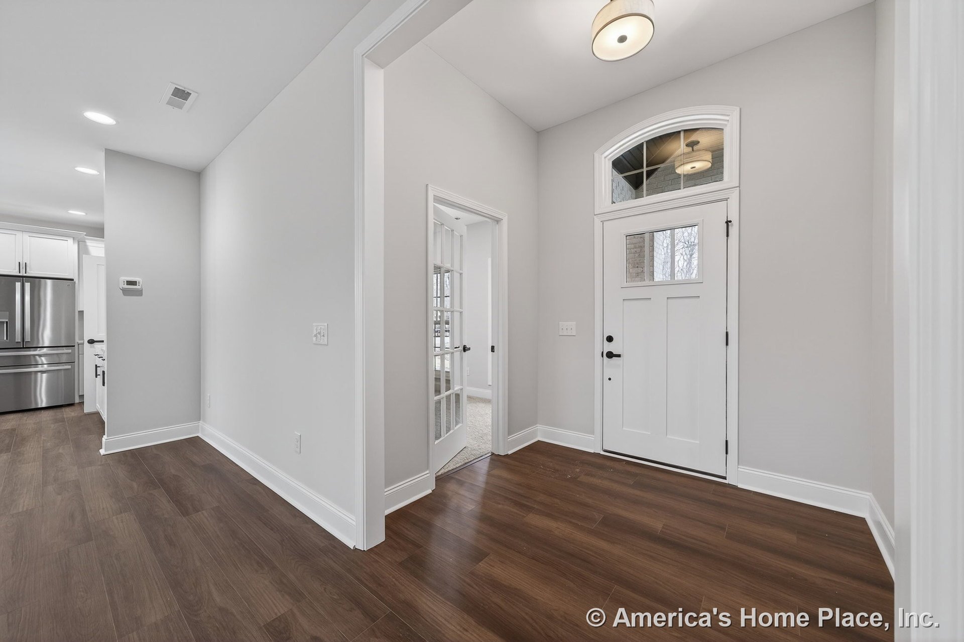 White paneled front door with arched transom window, wood-look plank flooring, wide baseboards, recessed ceiling light, glass French door leading to adjacent room, neutral wall
