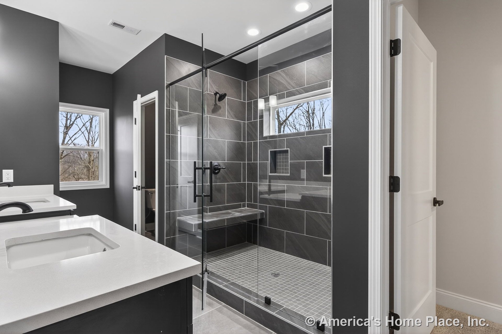 Double vanity with quartz countertops and modern fixtures, frameless glass shower enclosure with dark tile walls, built-in bench seat and shower niches, recessed ceiling lights