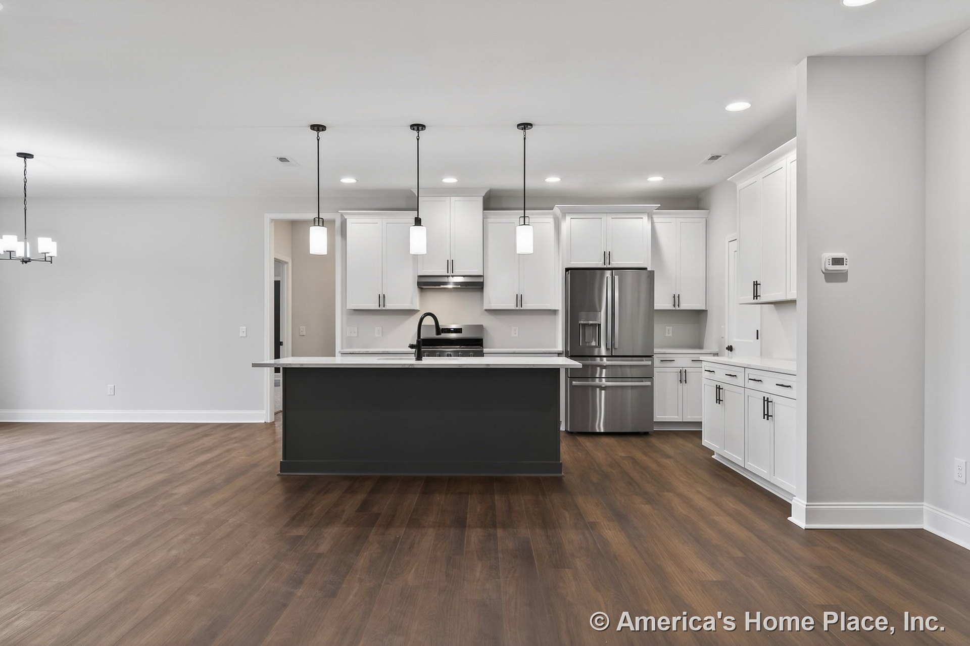 Open kitchen with white shaker cabinets, dark central island, stainless steel appliances, pendant lights above island, wood-look flooring, recessed lighting, solid surface