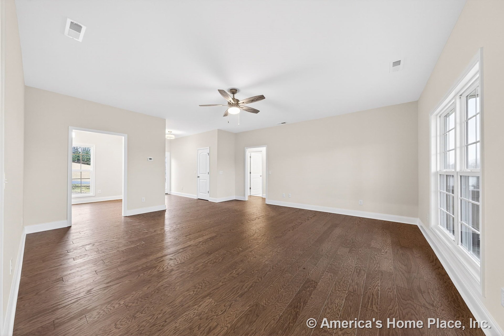 Wide plank hardwood flooring, large double-hung windows, ceiling fan with integrated light fixture, neutral wall paint, white baseboard trim, multiple interior doorways, and open