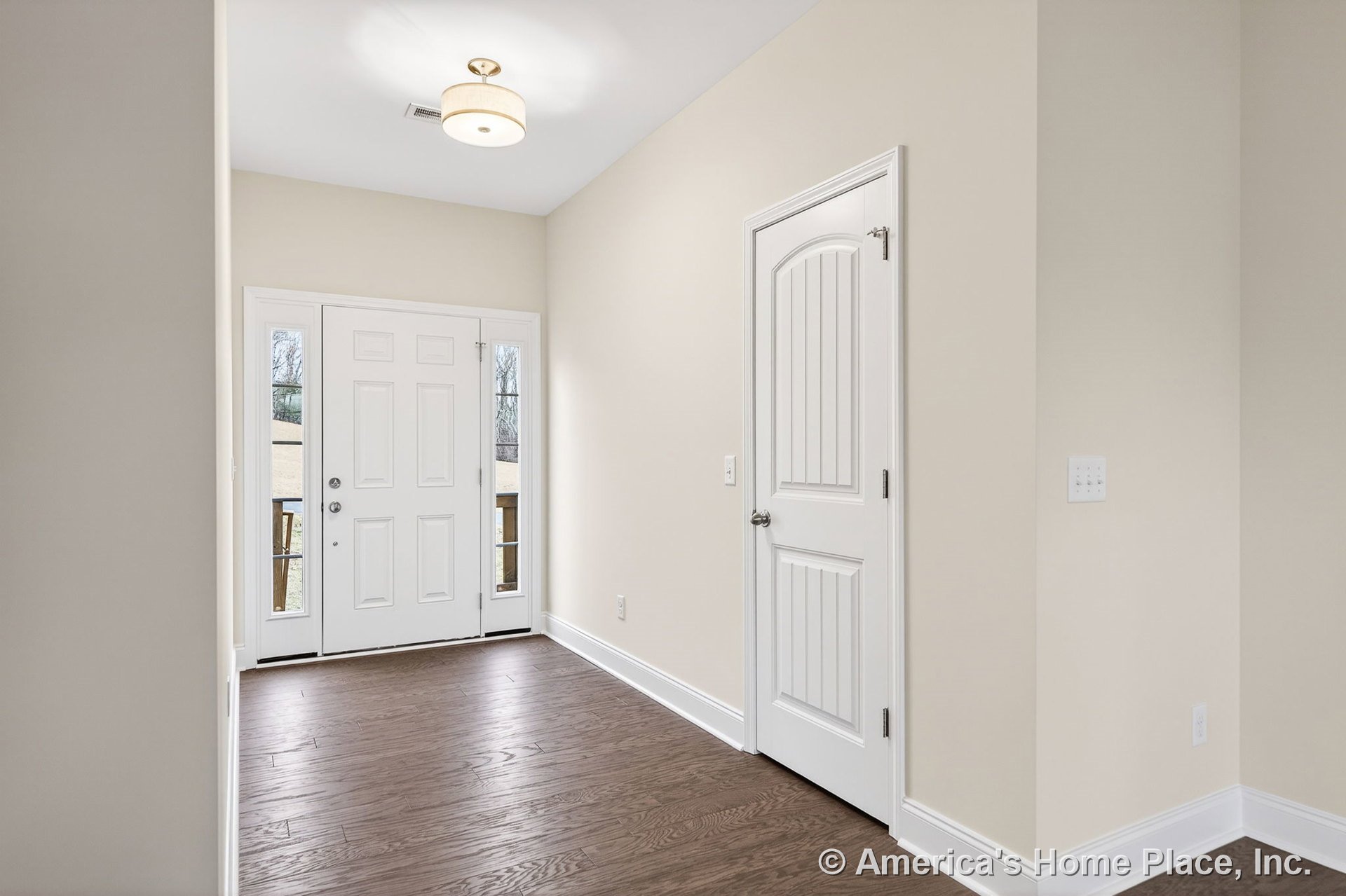 White paneled front door with sidelights, wood plank flooring, flush mount ceiling light, beige painted walls, wide baseboards and trim, white interior door with vertical panels