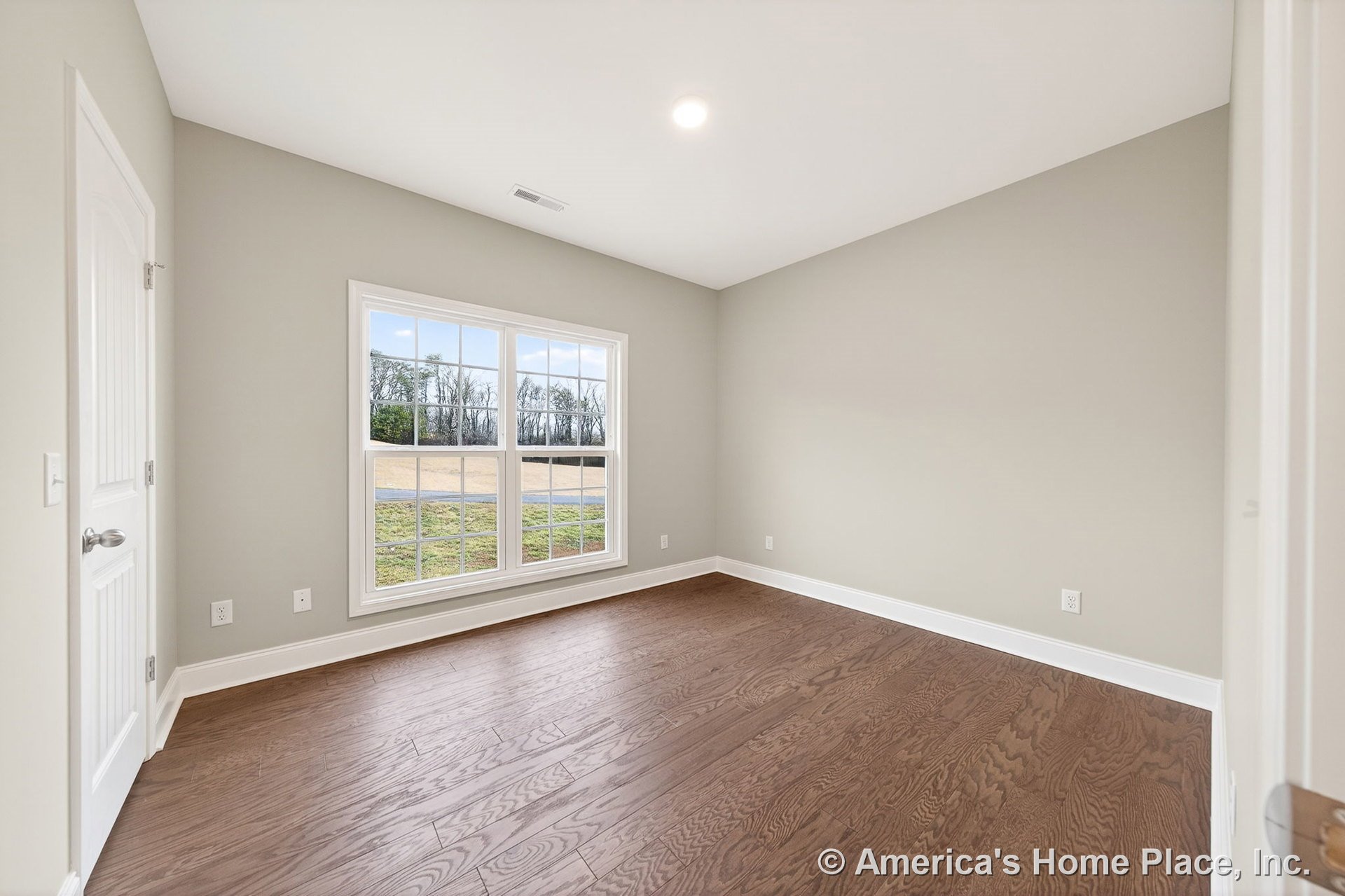 Bedroom with large double windows featuring grid pattern, light wood plank flooring, neutral painted walls, white baseboard trim, recessed ceiling light, paneled interior door