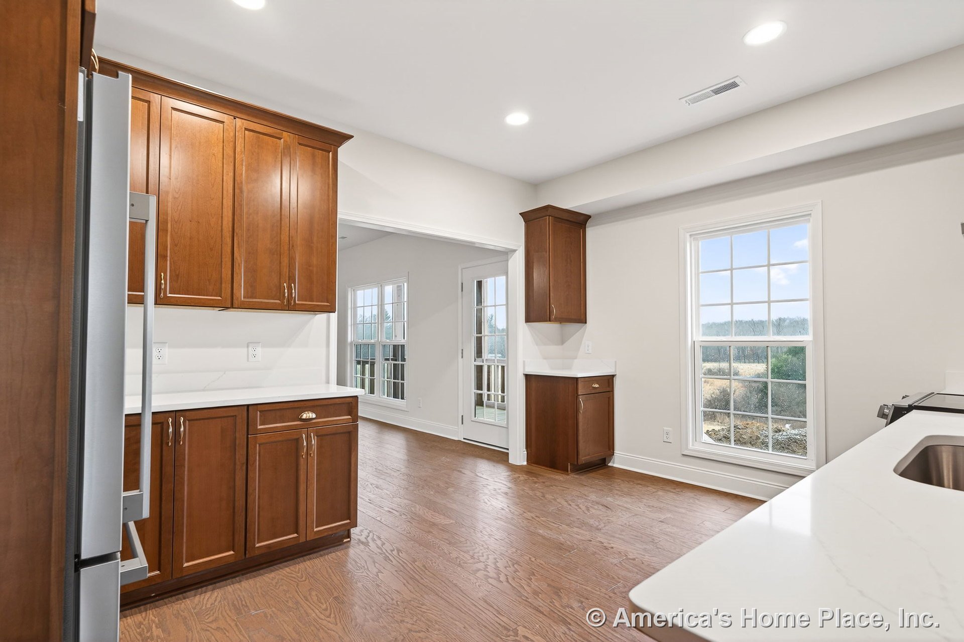 Wood cabinetry with upper and lower storage, white quartz countertops, wide plank hardwood flooring, large double-hung window, recessed ceiling lights, stainless steel sink, and