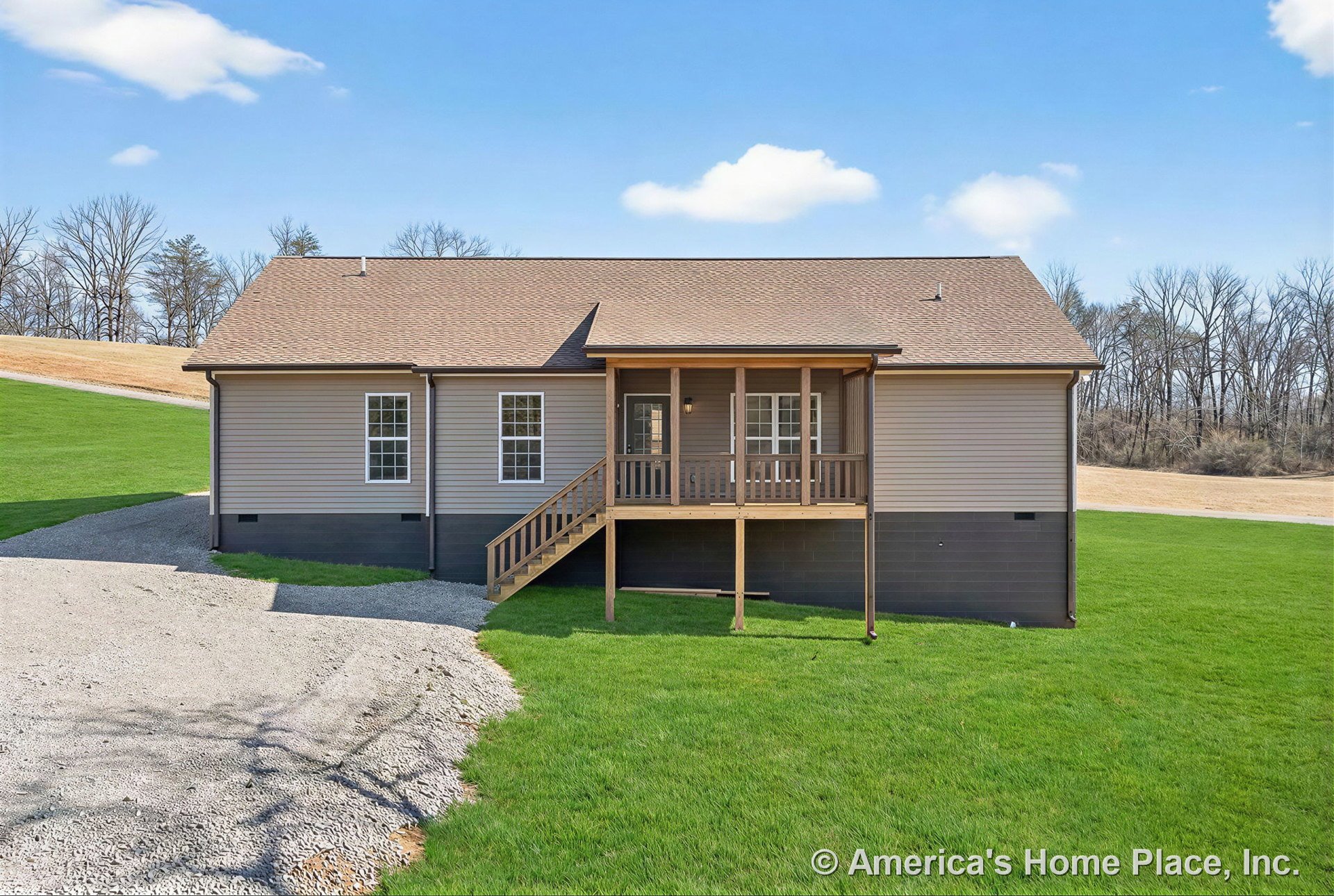 Covered front porch with wood railings and steps, tan vinyl siding exterior, gabled shingle roof, three double-hung windows, raised foundation, gravel driveway in rural setting.