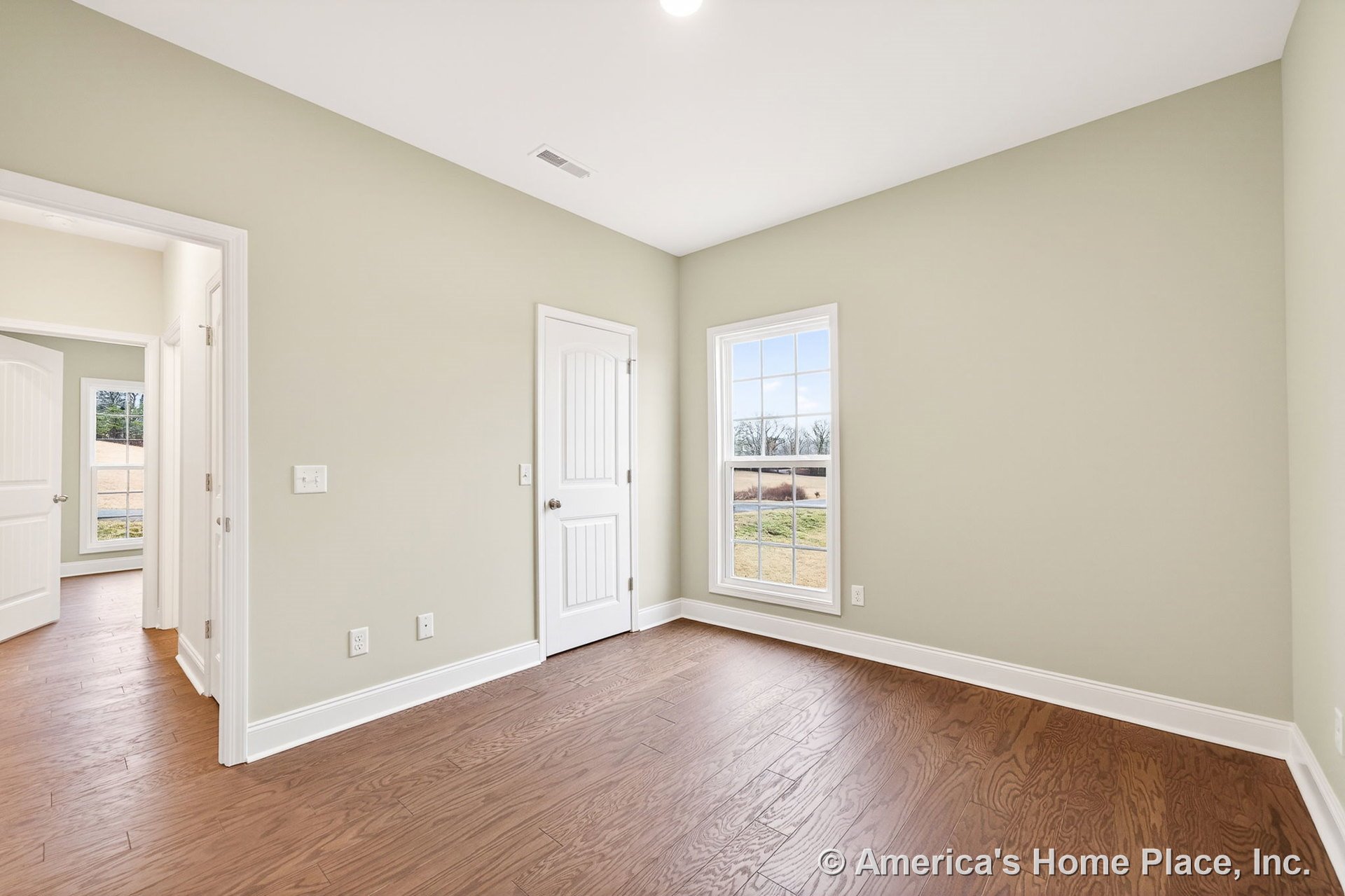 Bedroom with light green walls, white baseboards and door trim, wood plank flooring, large divided-pane window, white paneled interior doors, and recessed ceiling lighting.