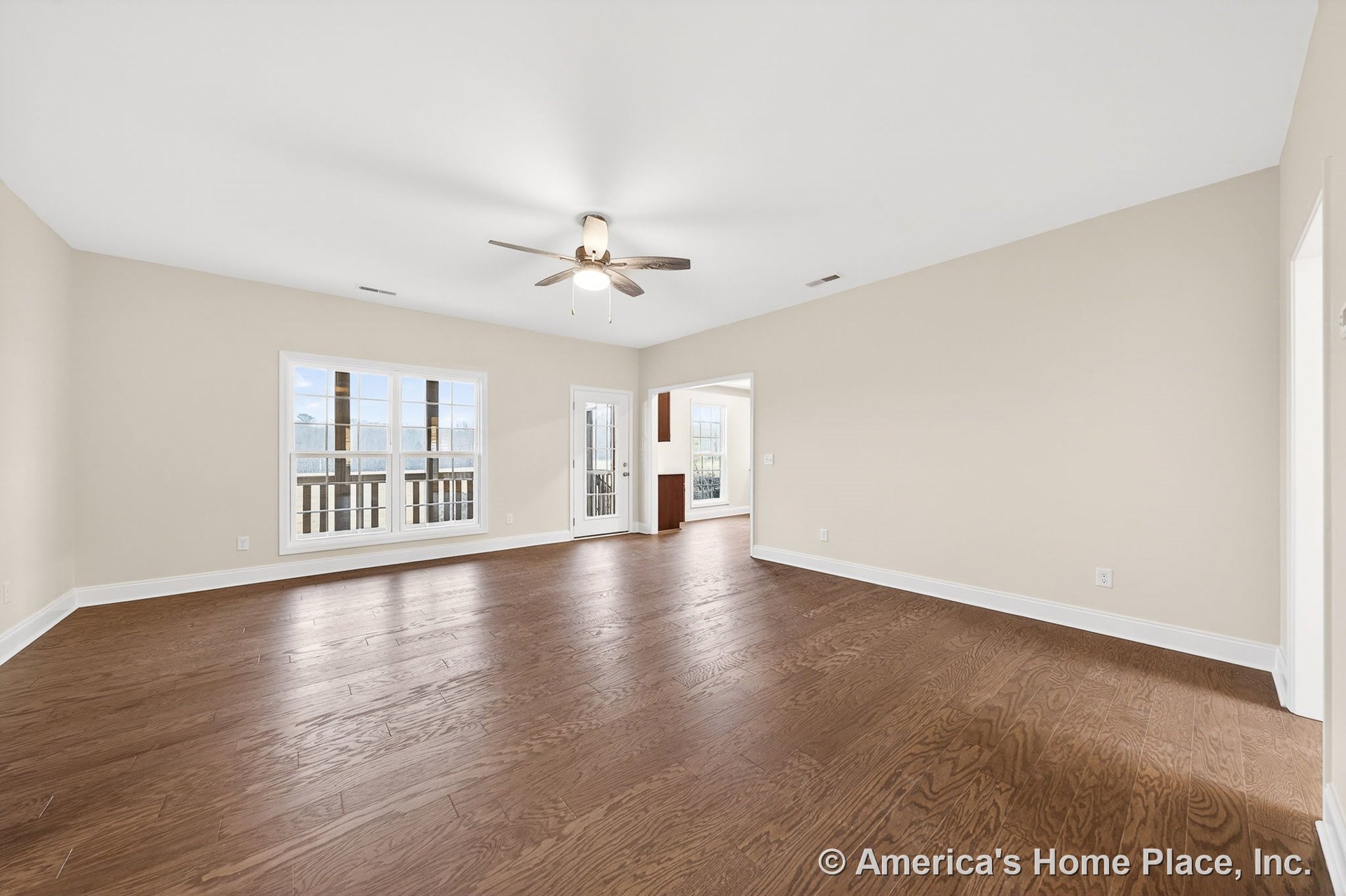 Wide plank hardwood flooring, ceiling fan with integrated lighting, large windows with white trim and baseboards, neutral wall color, glass exterior door, open living room layout