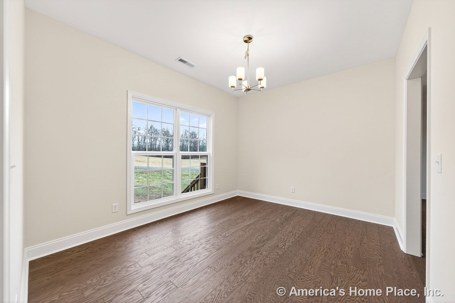 Dining room with large double windows framed in white trim, medium brown wood flooring, modern chandelier, neutral painted walls, white baseboards, and open doorway.