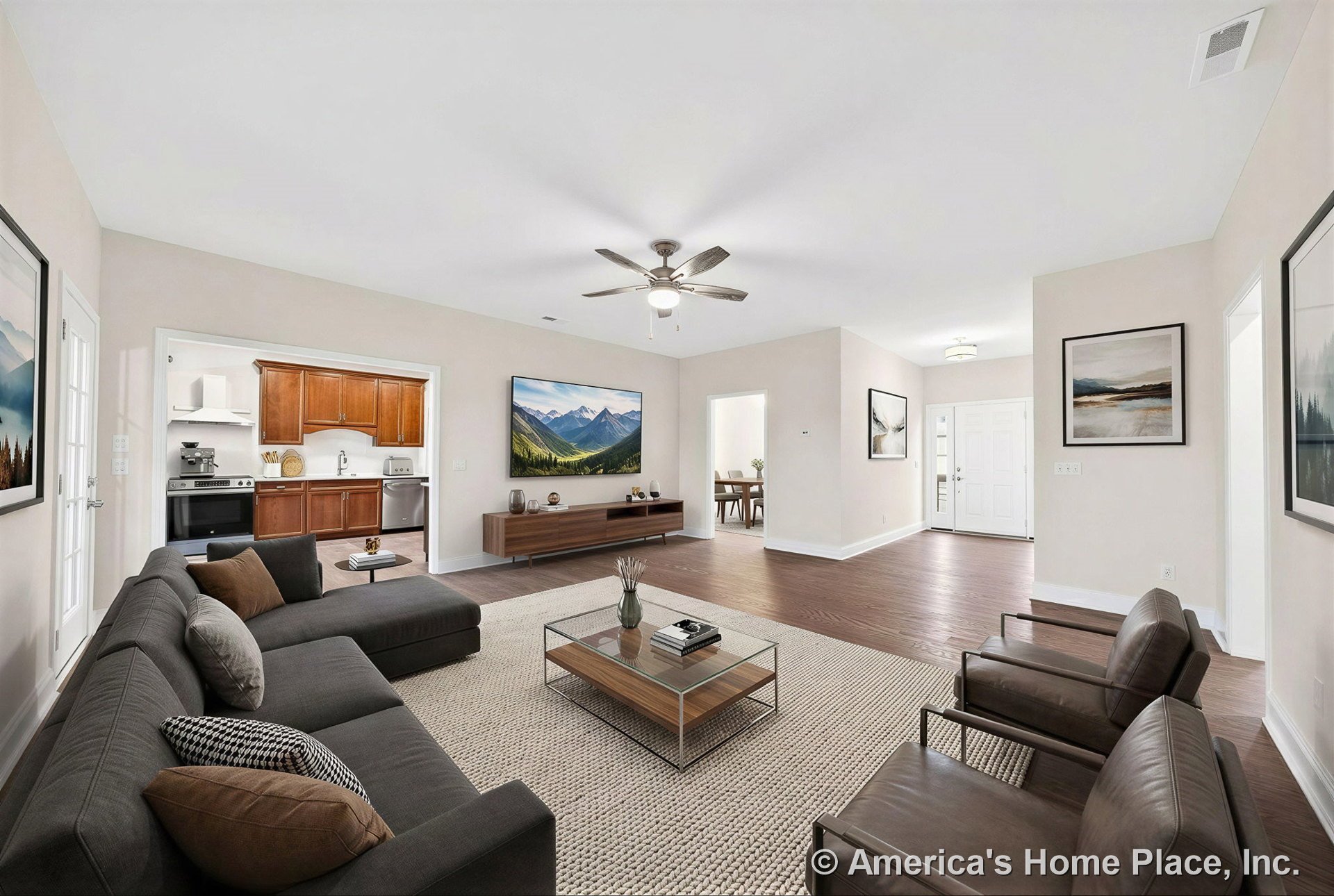Living room with wood flooring, ceiling fan and integrated light, white trim and baseboards, open floor plan leading to kitchen with wood cabinetry, large interior windows