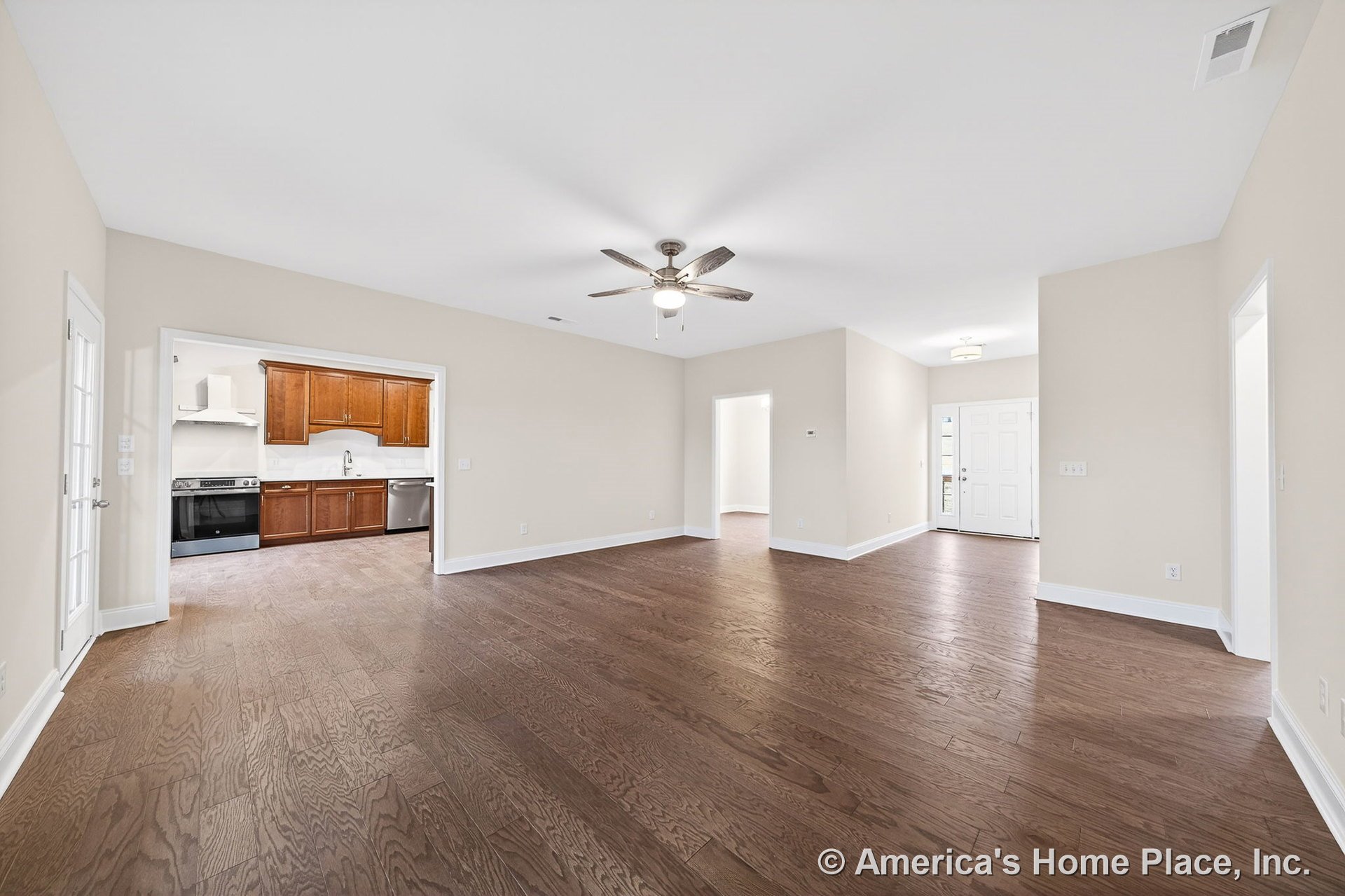 Open floor plan with hardwood flooring, white trim and baseboards, ceiling fan with light fixture in living area, entry foyer featuring overhead lighting, kitchen equipped with