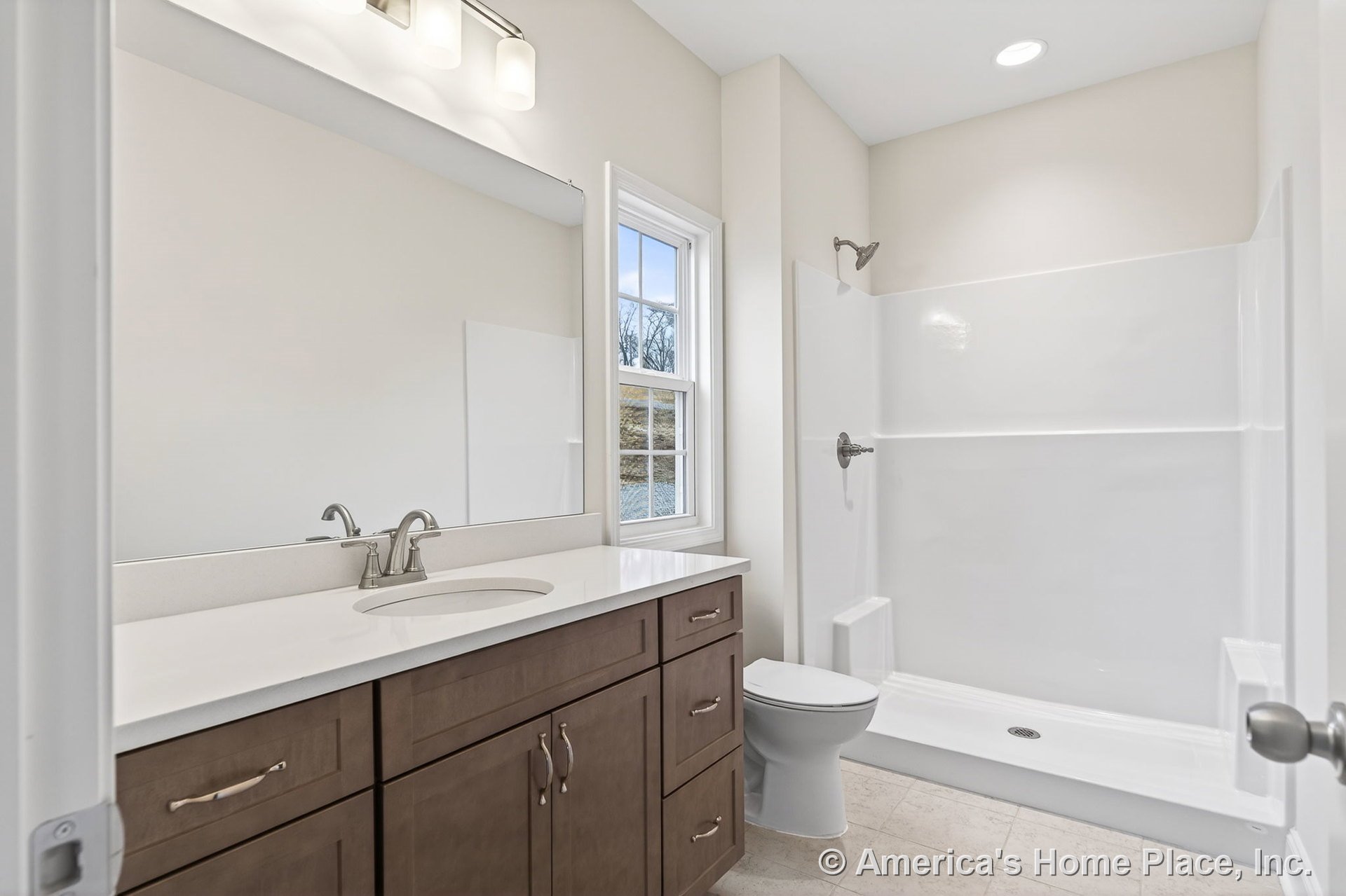 Walk-in shower enclosure with glass door, dark wood vanity cabinetry topped by stone countertop and undermount sink, large wall mirror, tile flooring, window with white trim