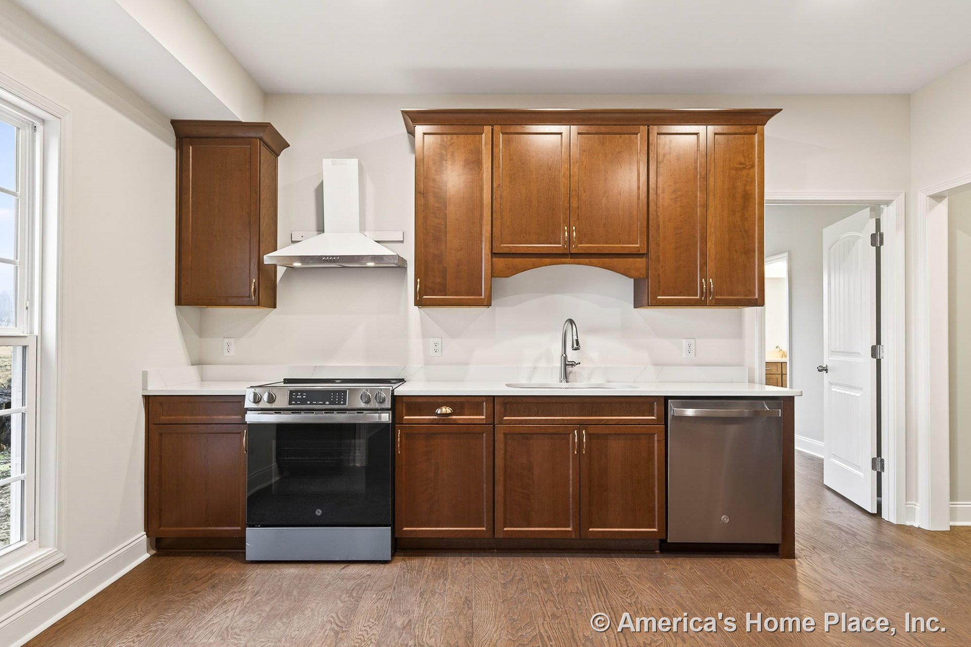 Wood cabinetry with upper and lower storage, stainless steel range and hood, quartz countertops, single handle faucet, built-in dishwasher, hardwood flooring, window trim, recessed