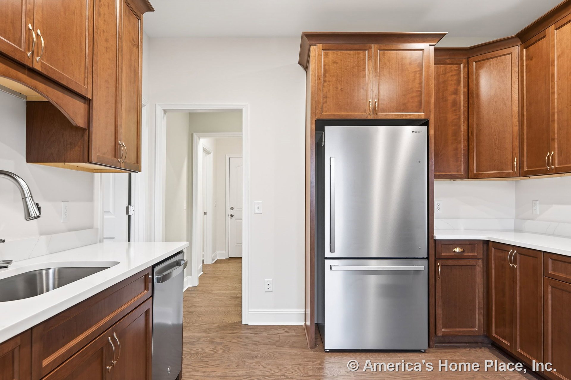 Custom kitchen with wood upper and lower cabinets, white solid surface countertops, stainless steel refrigerator and dishwasher, undermount sink with gooseneck faucet, and hardwood