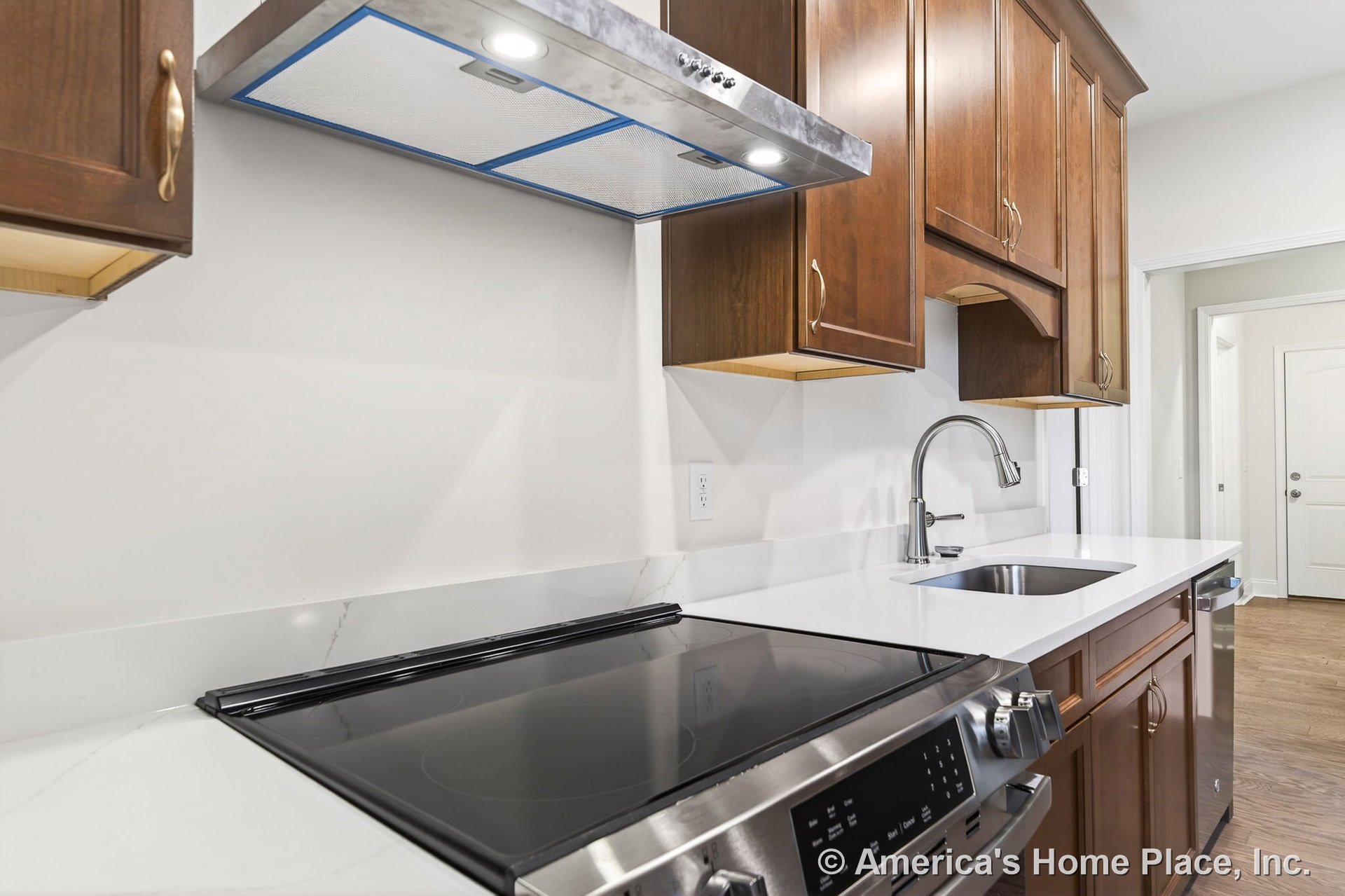 Wood cabinetry kitchen with white quartz countertops, electric cooktop, stainless steel range hood, undermount sink, modern faucet, built-in stainless steel appliances, upper and