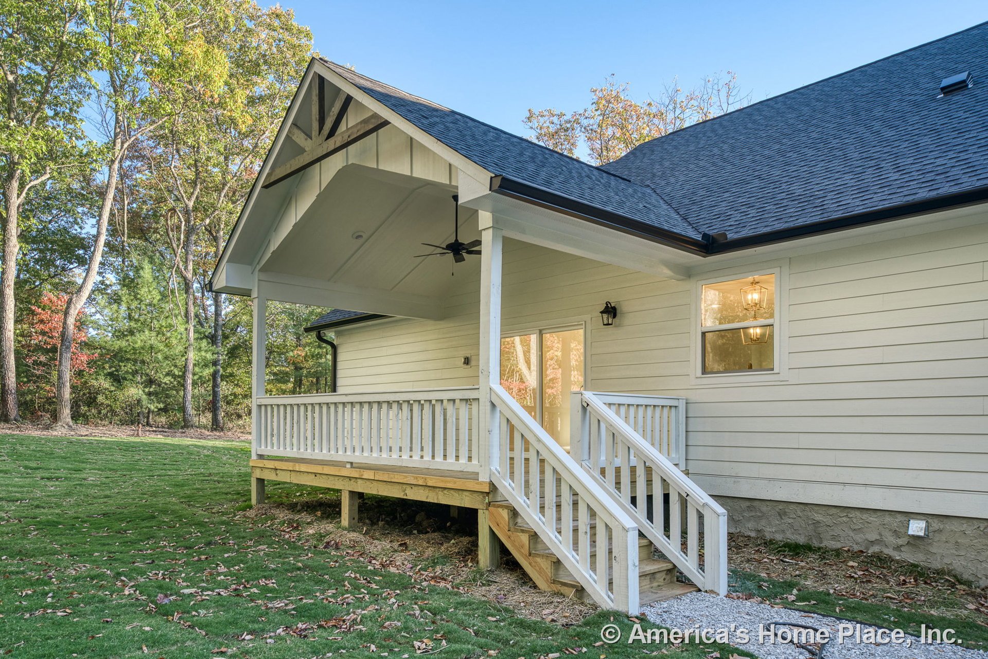 Covered back porch with white wood railing, ceiling fan, exterior siding, gable roof, back steps, windows, door, and decorative trim.