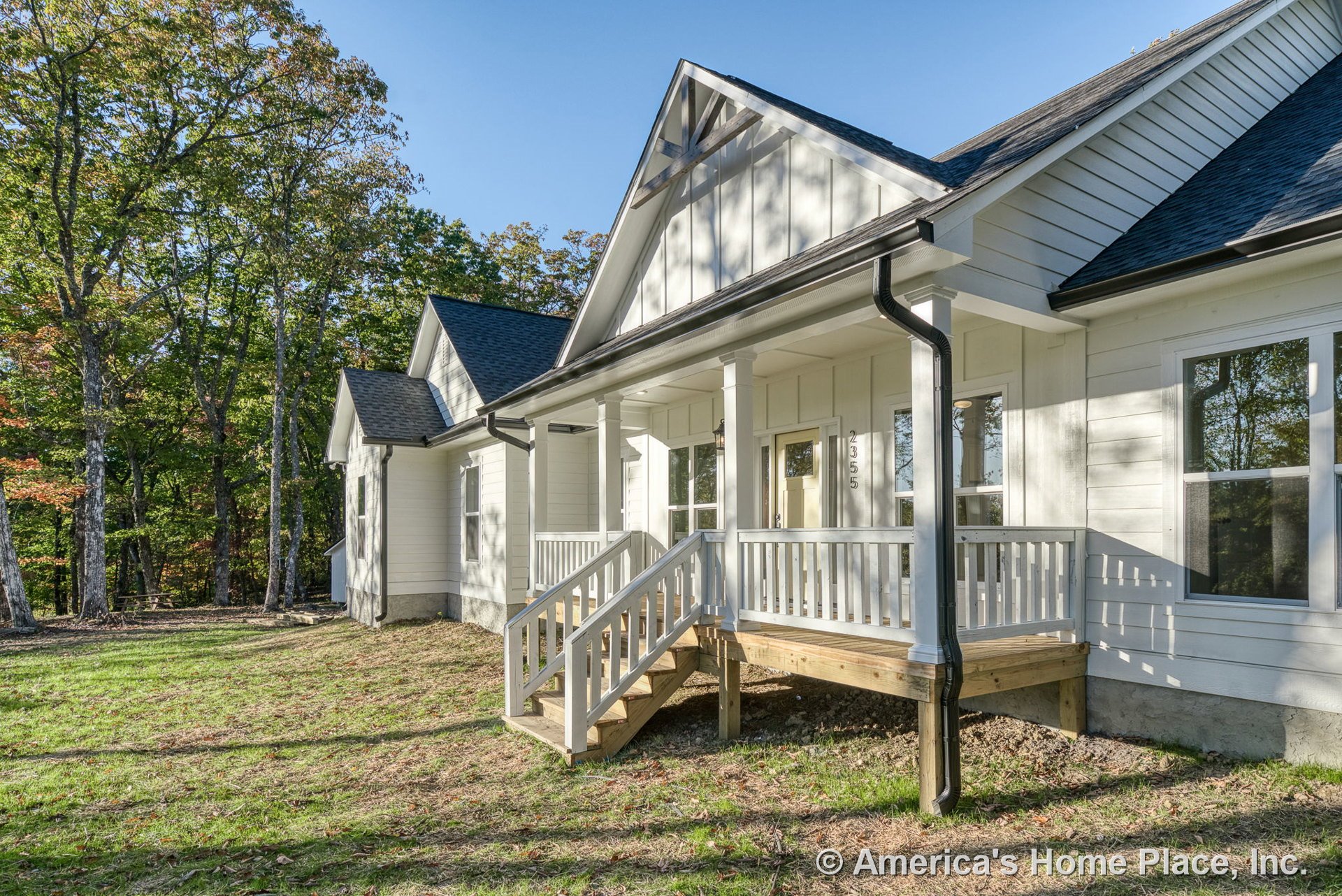 Covered front porch with white railings and columns, wooden steps, white horizontal siding, black asphalt shingle roof, decorative gable trim, and white framed windows.