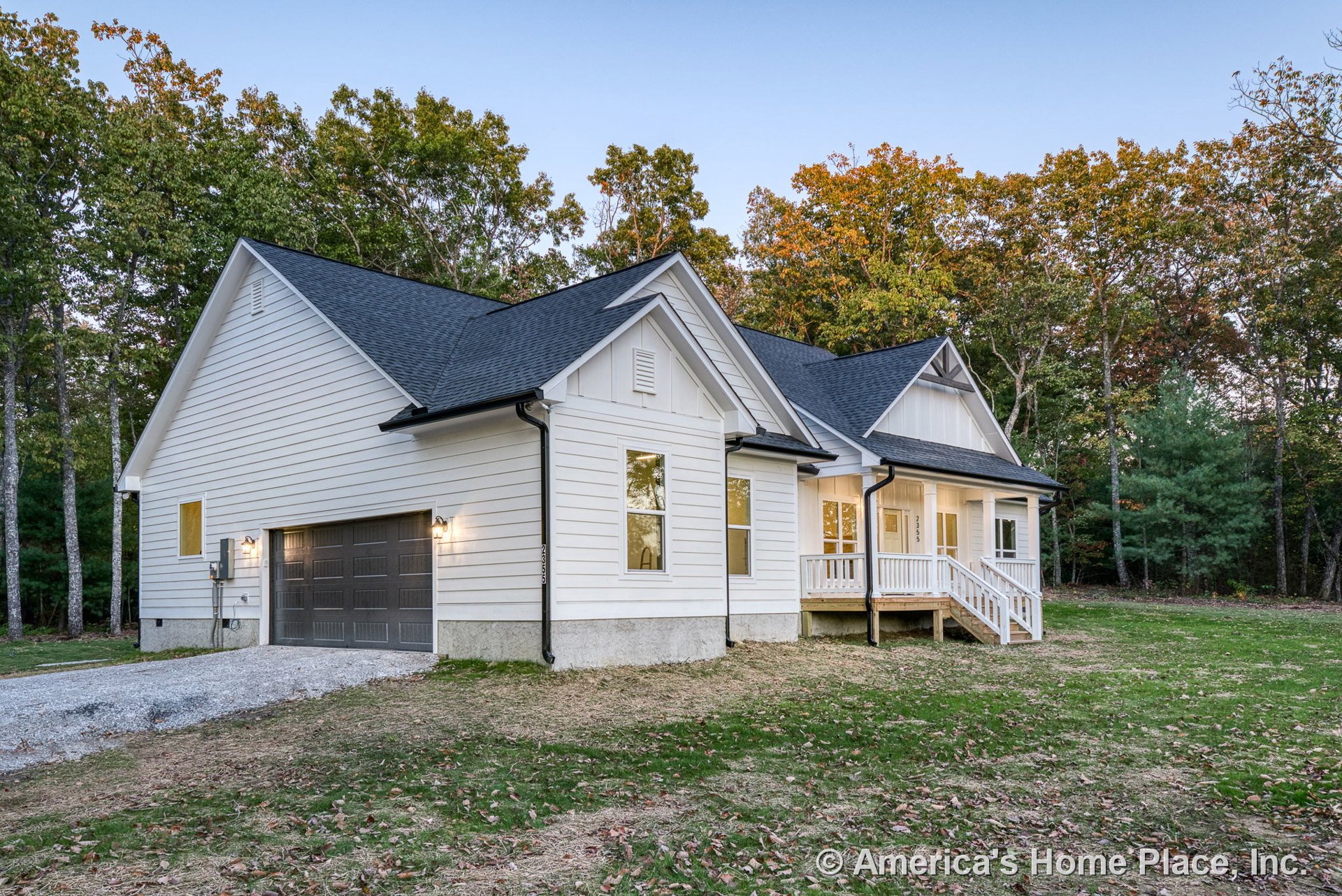 White horizontal siding exterior with covered front porch, paneled two-car garage, black shingle roof, double-hung windows, wall-mounted lighting, white trim, entry steps, railing