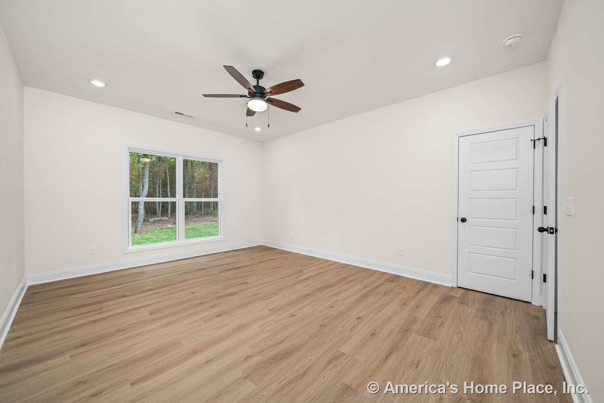 Bedroom with light wood plank flooring, large double window, white paneled door, ceiling fan with built-in light, recessed ceiling lights, white baseboards, and neutral walls.