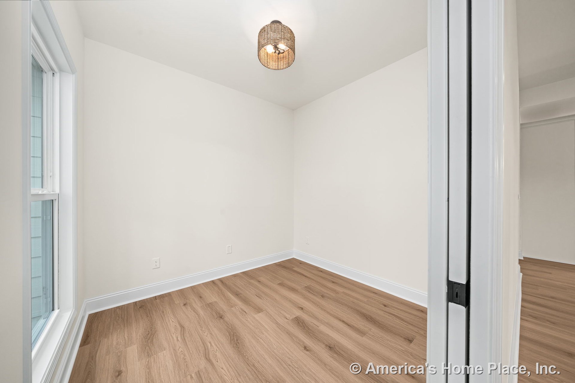 Small bedroom with light wood plank flooring, white baseboards and trim, large window allowing natural light, sliding closet door, neutral painted walls, and woven ceiling light