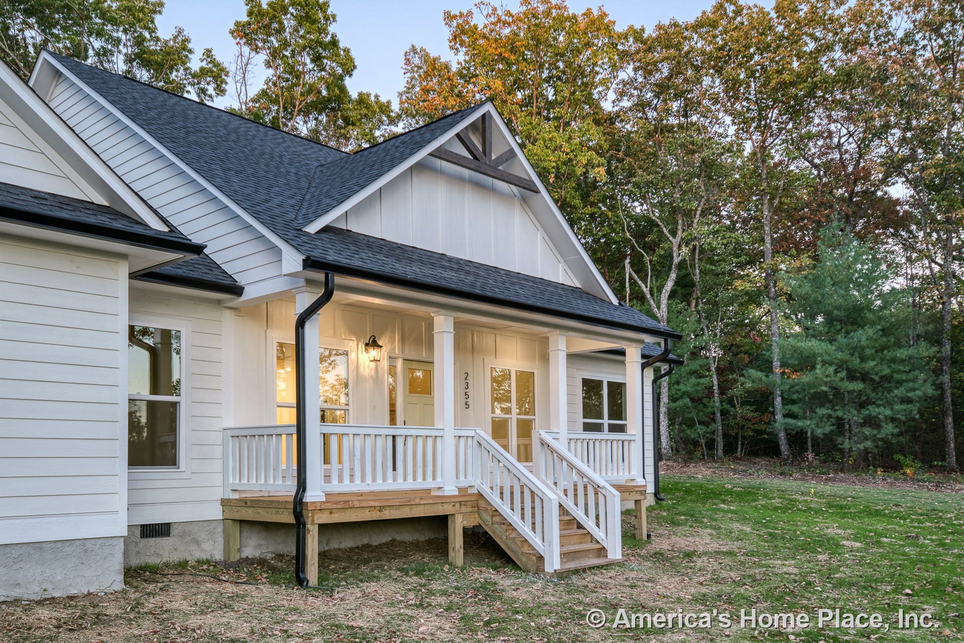 Covered front porch with white railings and columns, wooden steps leading to entry door, white horizontal siding, black shingle roof, double front windows, exterior wall lantern