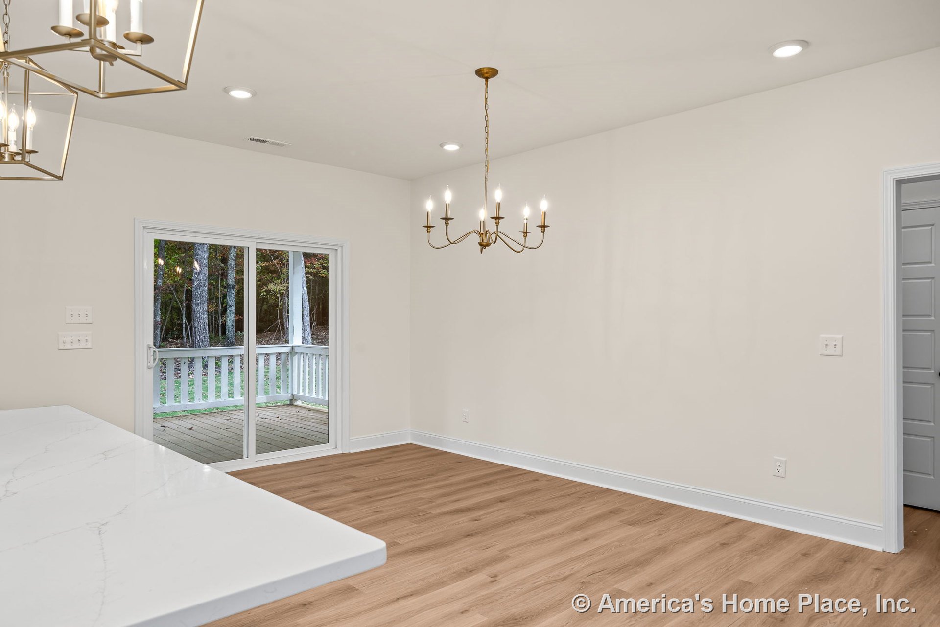 Brass chandelier and recessed ceiling lights illuminate dining area with light wood flooring, neutral walls, and baseboard trim; sliding glass doors lead to covered porch with
