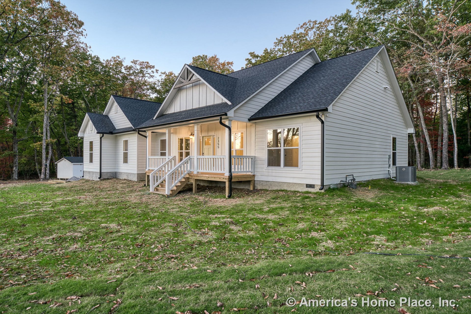 Covered front porch with white railing and steps, white horizontal siding, multiple gabled rooflines with black shingles, double-hung windows with white trim, exterior lighting