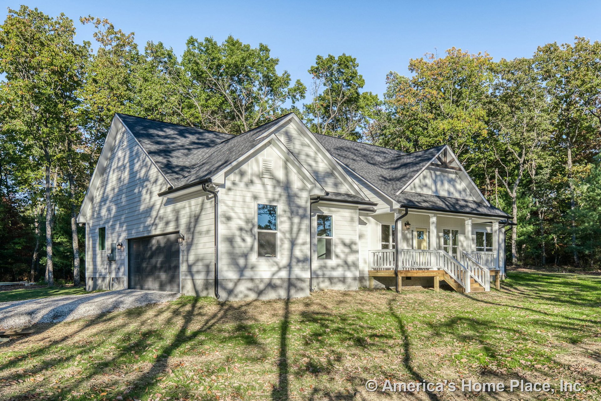 Light horizontal siding with white trim, covered front porch with steps and railing, attached garage featuring dark doors, dark roof shingles, exterior lighting fixtures, multiple