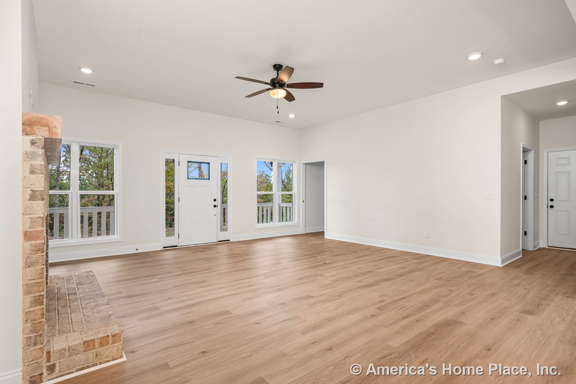 Light wood plank flooring, brick fireplace hearth, white trim and baseboards, large double windows, ceiling fan with light, recessed ceiling lights, neutral walls, open layout, and
