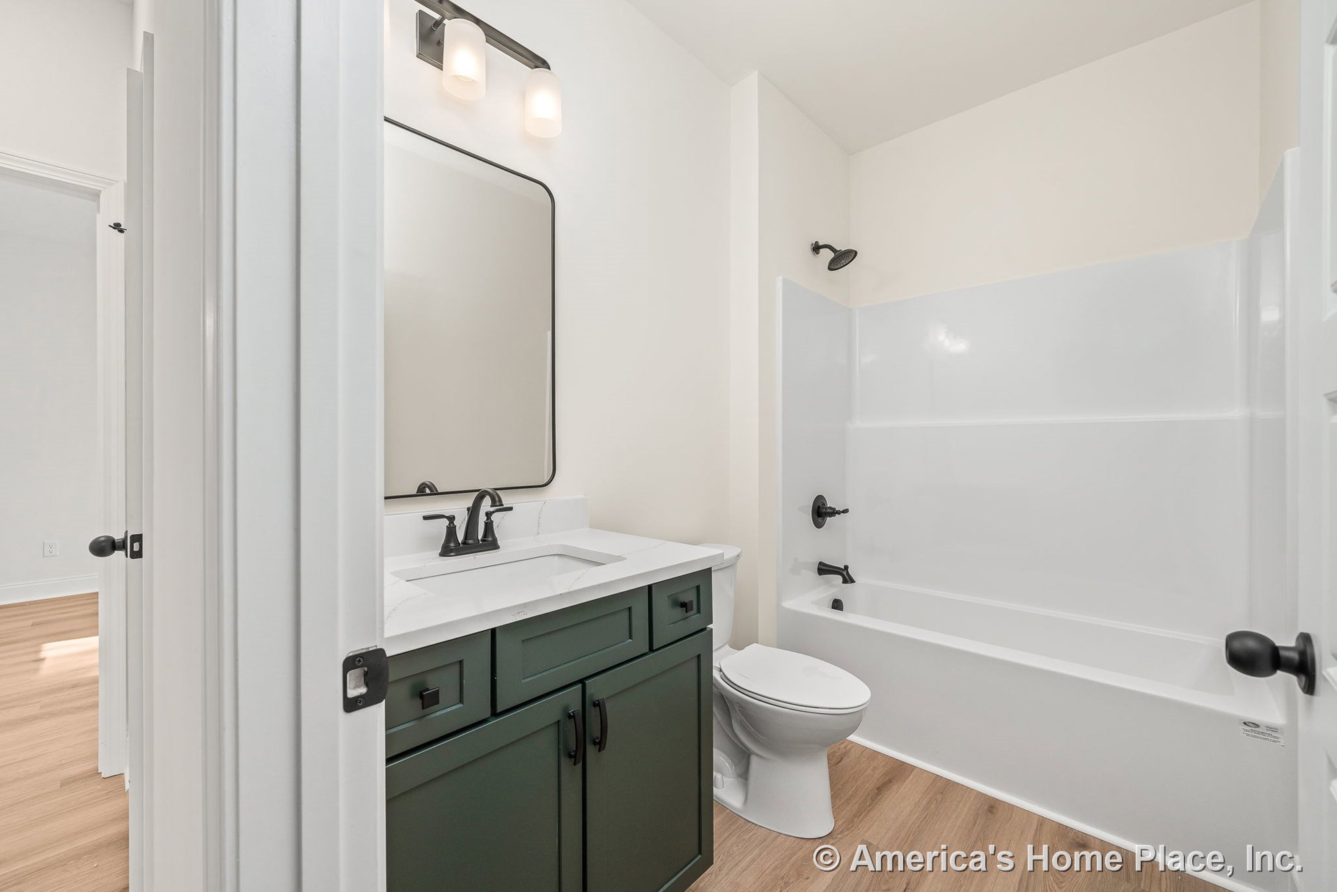 Green shaker-style vanity with white quartz countertop and matte black faucet, single sink, wall mirror, wall-mounted vanity light, tub-shower unit with white surround, light