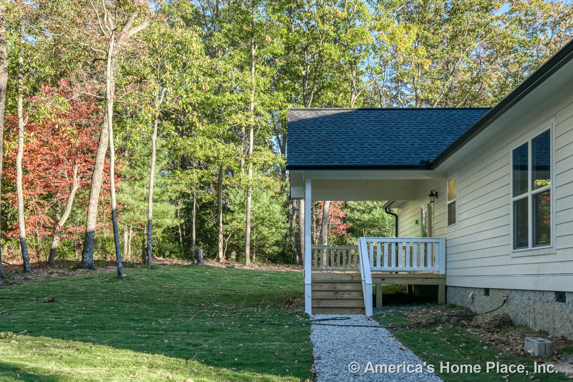 Covered front porch with white railings, horizontal siding, gravel walkway, wooden steps, double-hung windows, and dark shingle roof.
