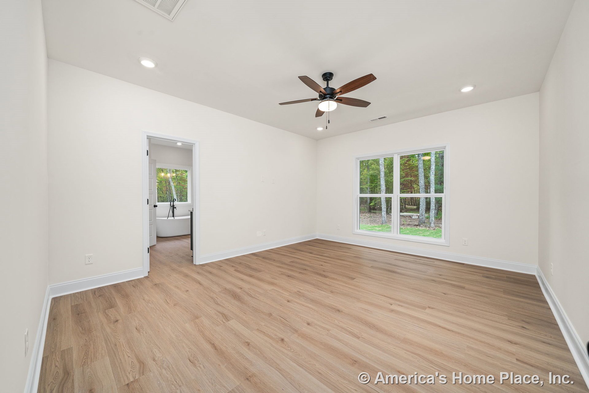 Bedroom with light wood plank flooring, white trim and baseboards, large double window providing natural light, ceiling fan with integrated light fixture, recessed ceiling lights