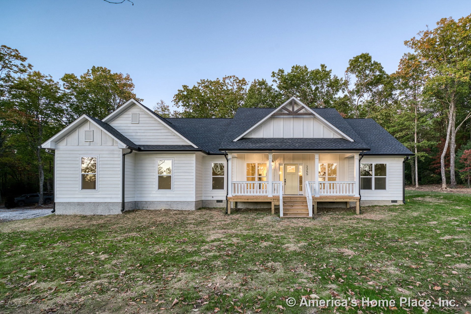 Covered front porch with white railings, board-and-batten siding on the gable, multiple double-hung windows, black shingle roof, and wooden entry steps.